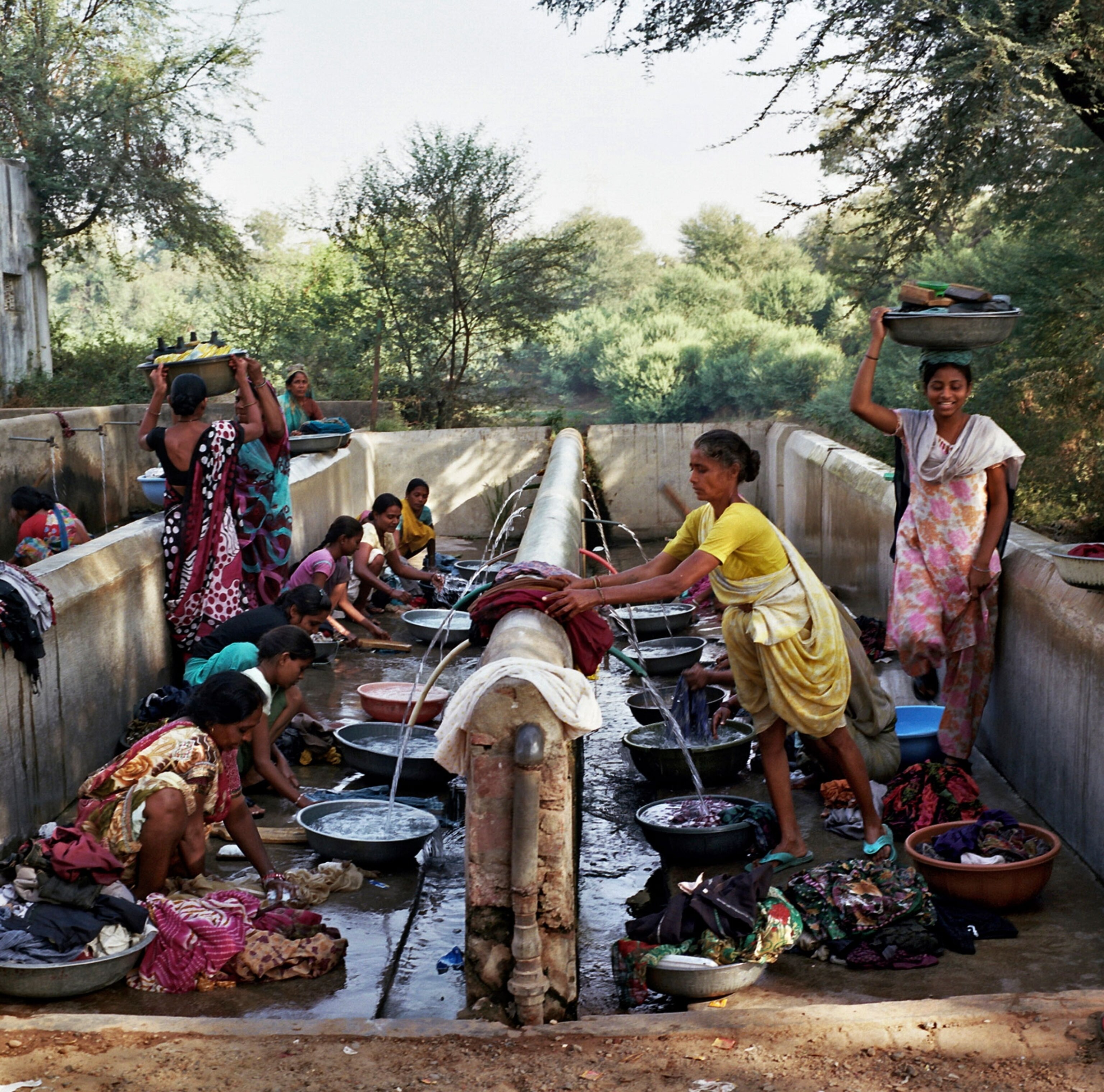 Dressed in colorful clothing, women from the Self-Employed Women's Association wash clothes in a communal area outside under green trees