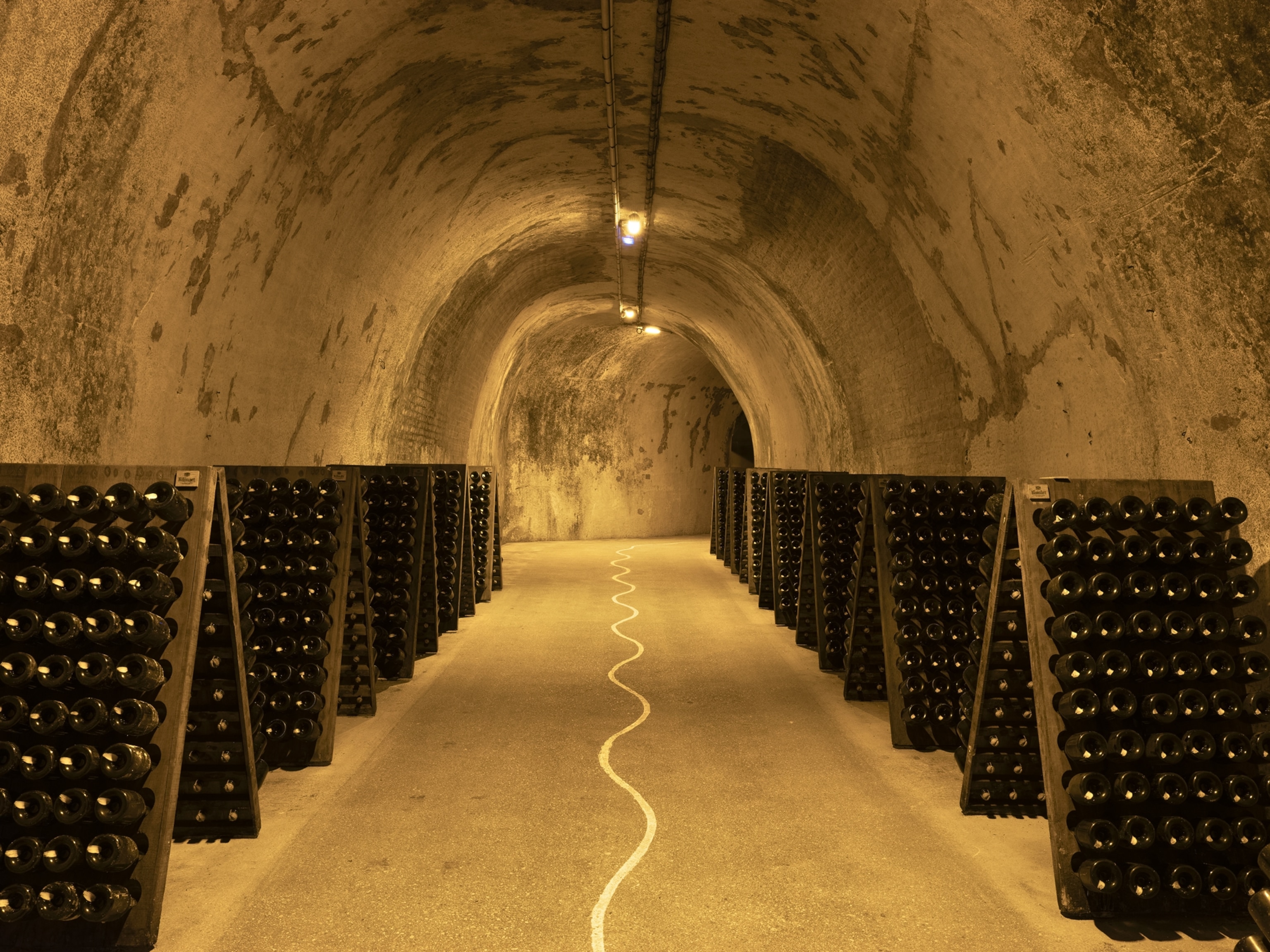 Wooden bottle racks hold rows of wine bottles inside the crayères cellar at Ruinart Champagne, a former chalk quarry in Reims, France.