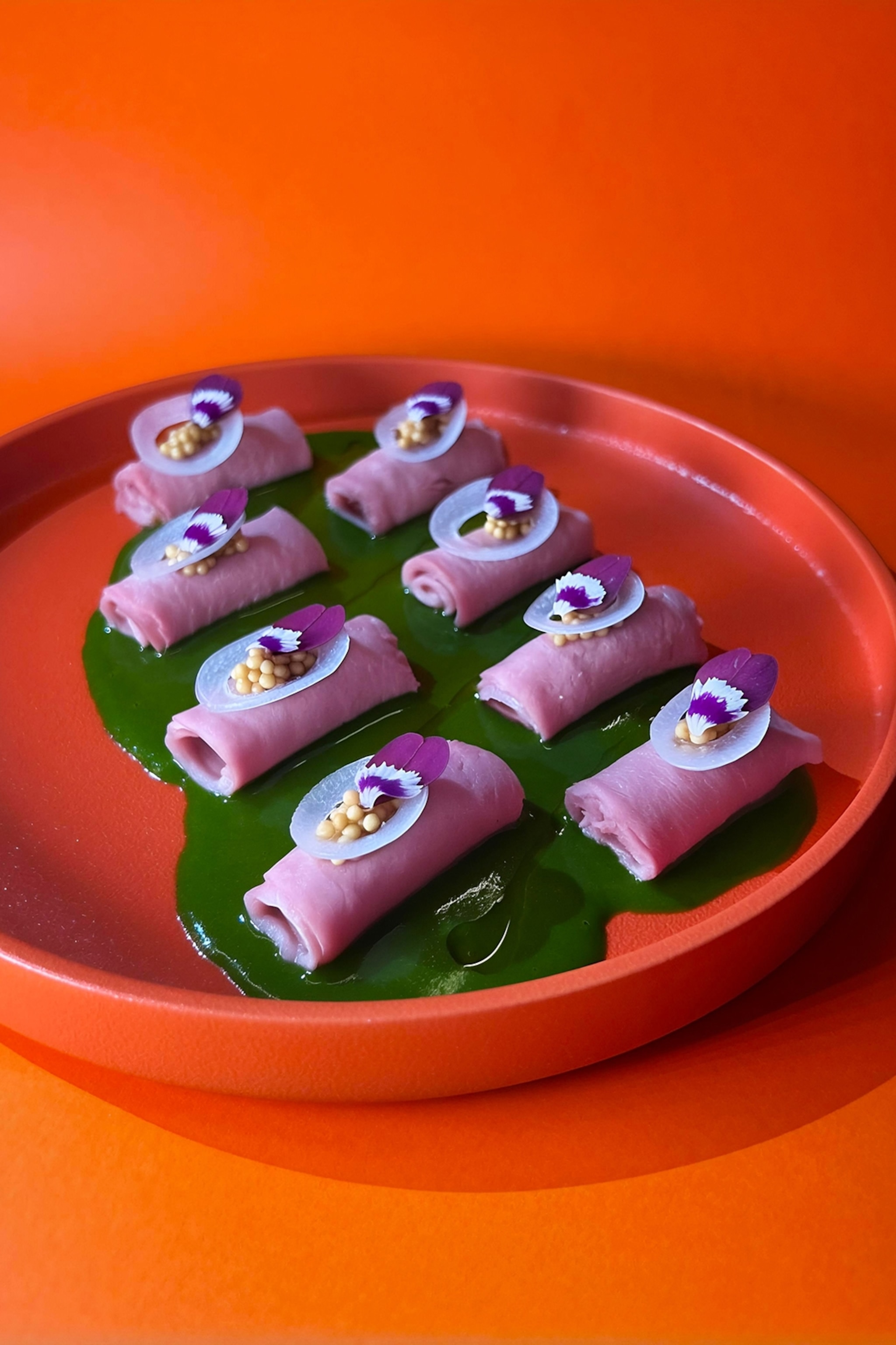 A close-up on a dish of small rolls of duck meat with a purple sauce over the top.