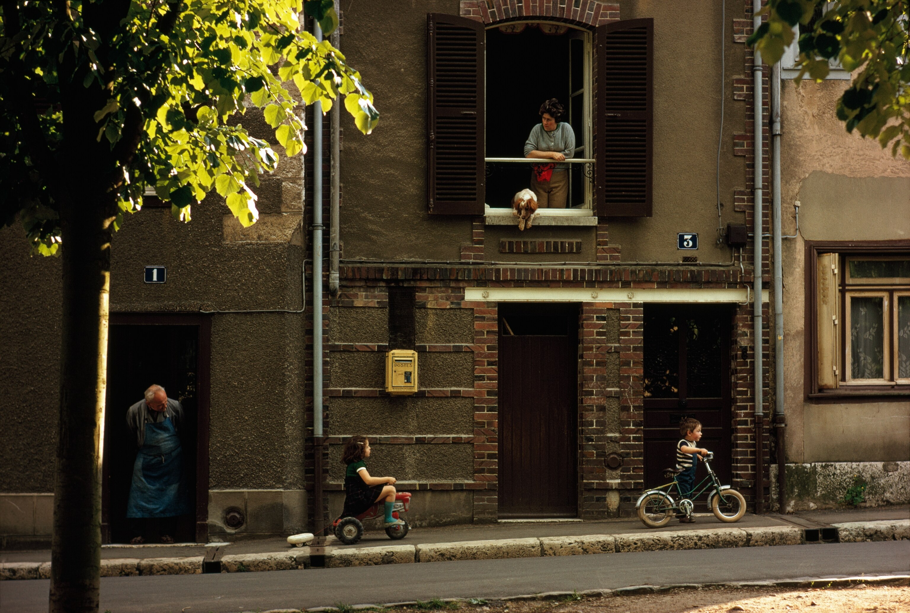 Under the watchful eye of elders, children ride bicycles on a sidewalk in Chartres, France. The city is home to the iconic Notre-Dame de Chartres Cathedral, a UNESCO World Heritage site. This cathedral features 12th- and 13th-century stained-glass windows, which represent the height of Gothic art in France.