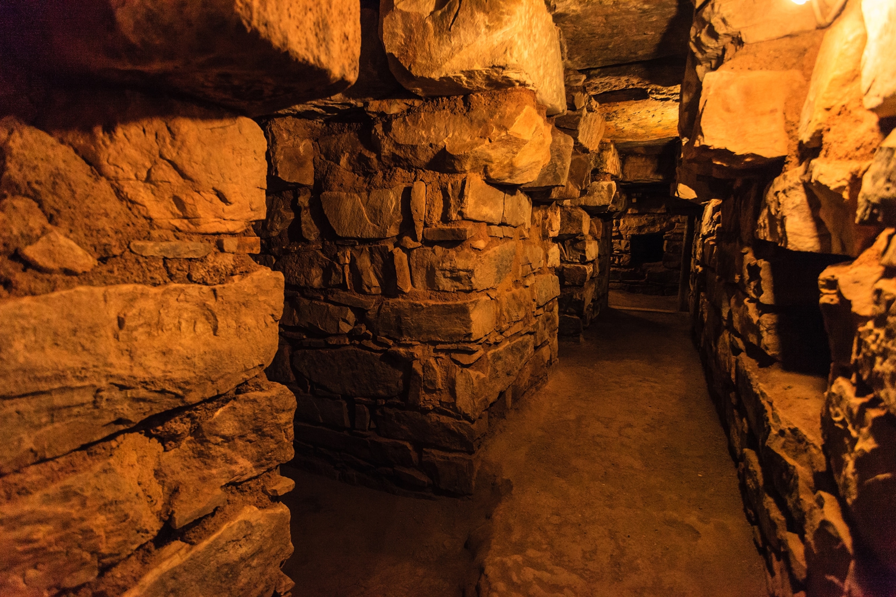 Internal corridor made of stone dimly lit by orange tinted lighting