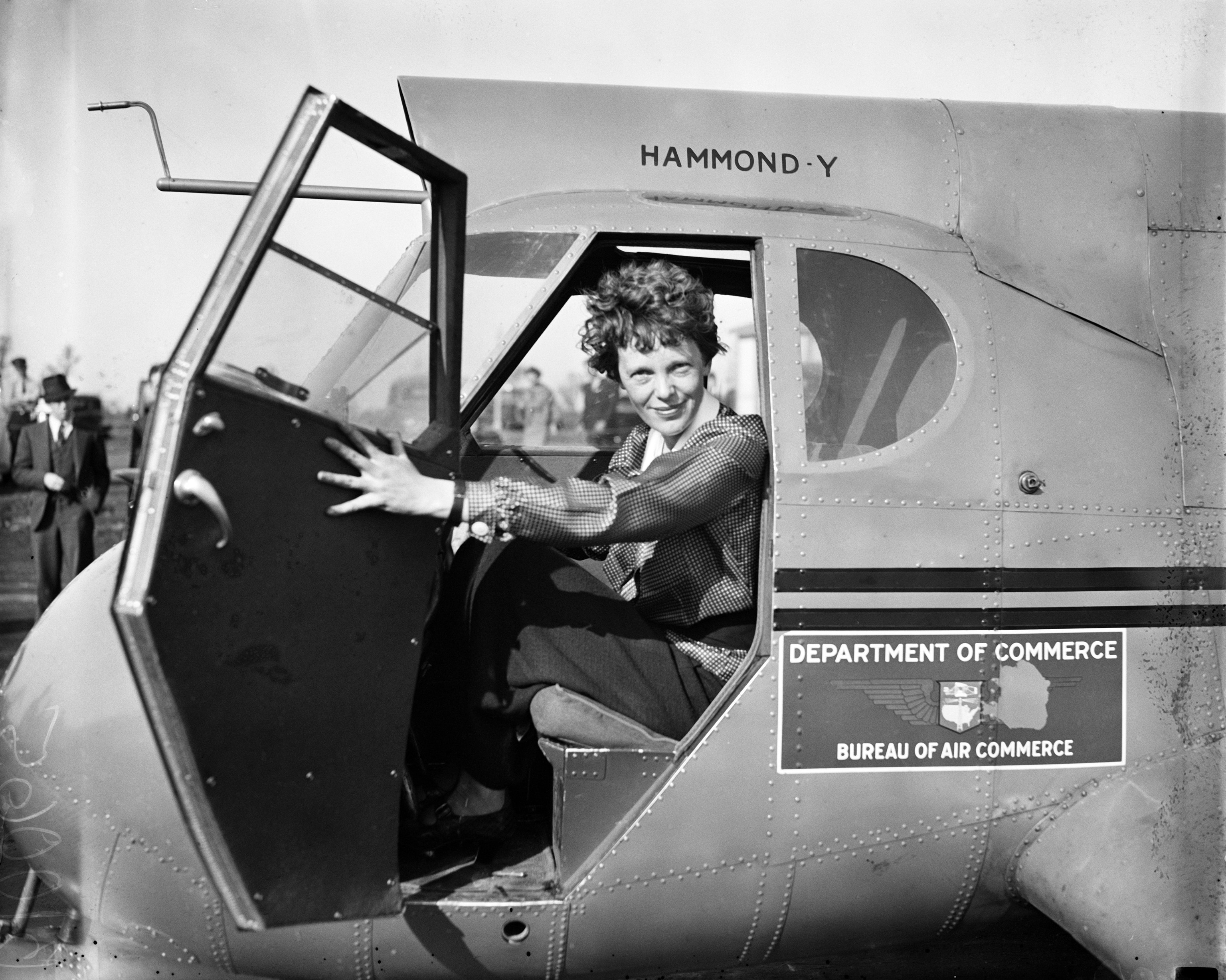 A black and white photograph of a woman opening the cockpit door of a plane.