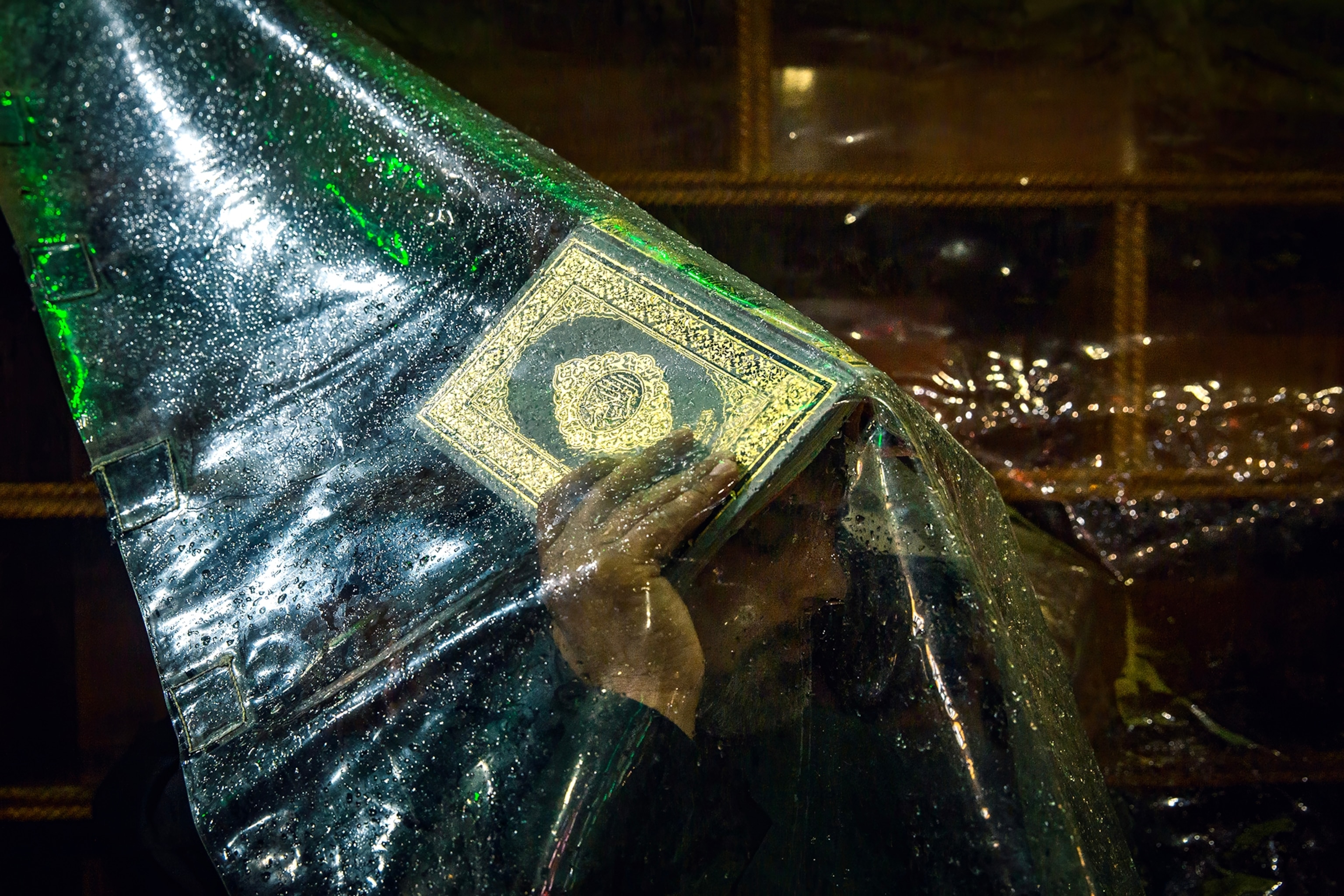 A man holds a gilded book over his head beneath a sheet of plastic.