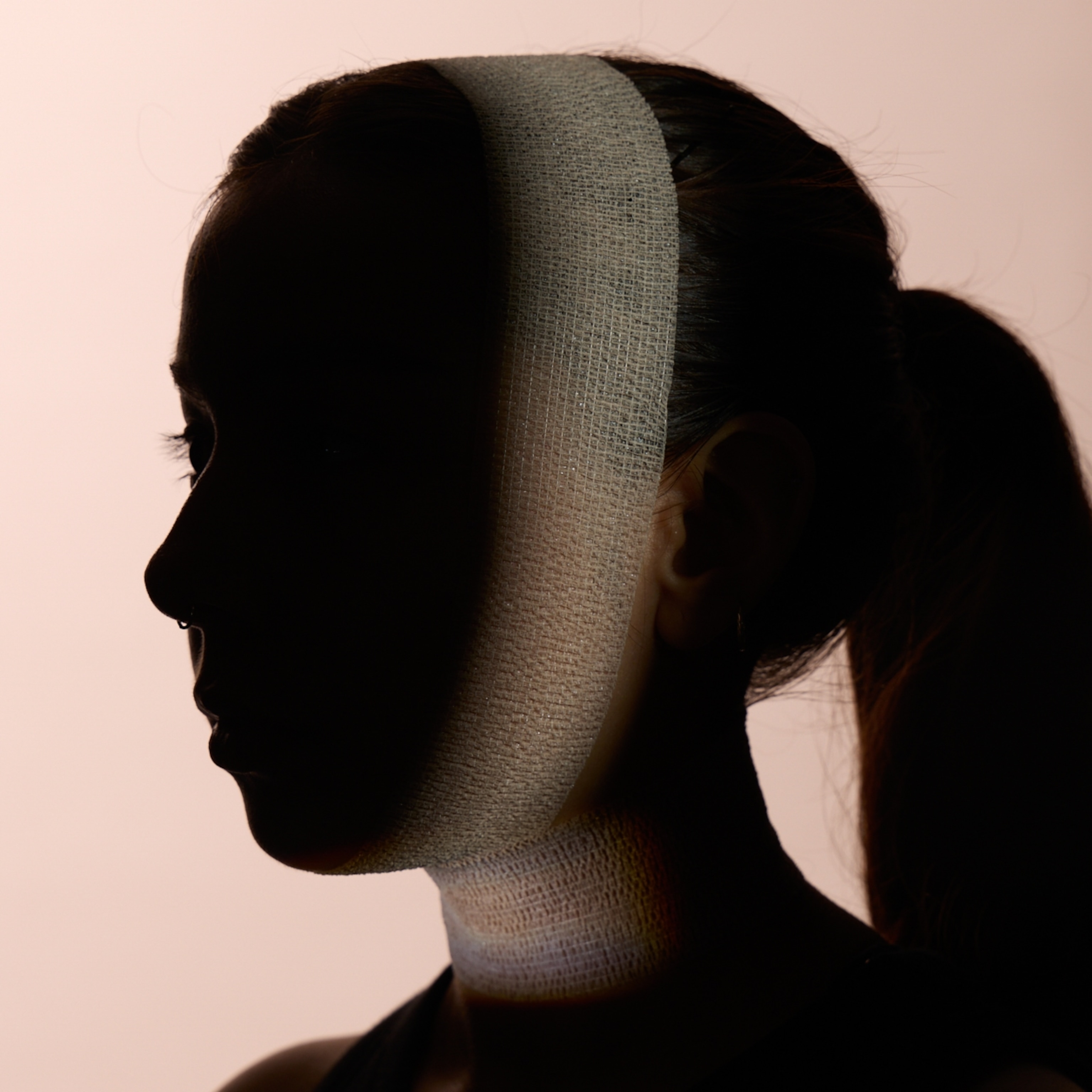 A silhouette of a woman's bust with a wrap around her jaw and neck, which is lit by a spot light