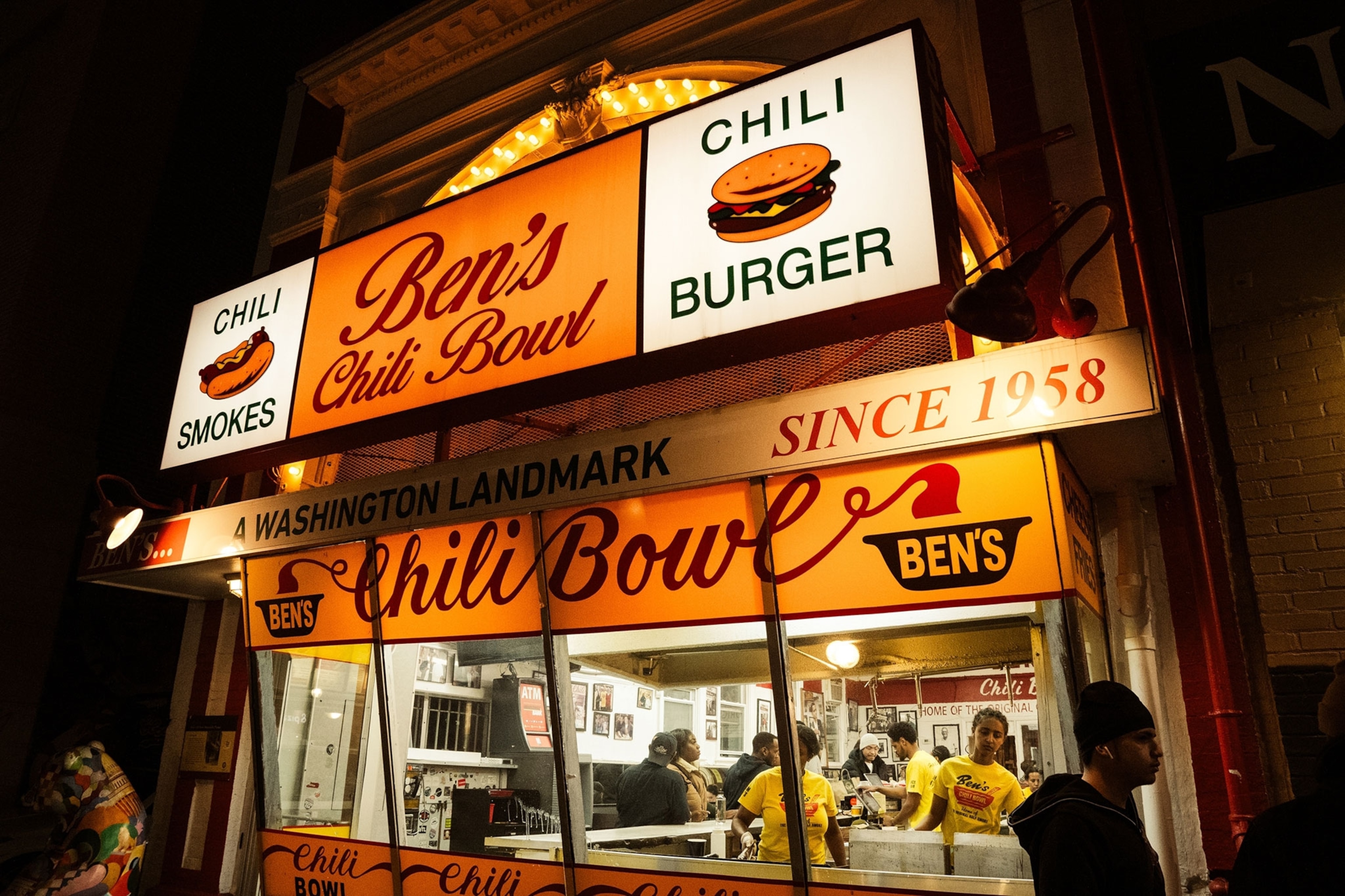 An orange hue illuminates the sign, on top of a building with people inside.