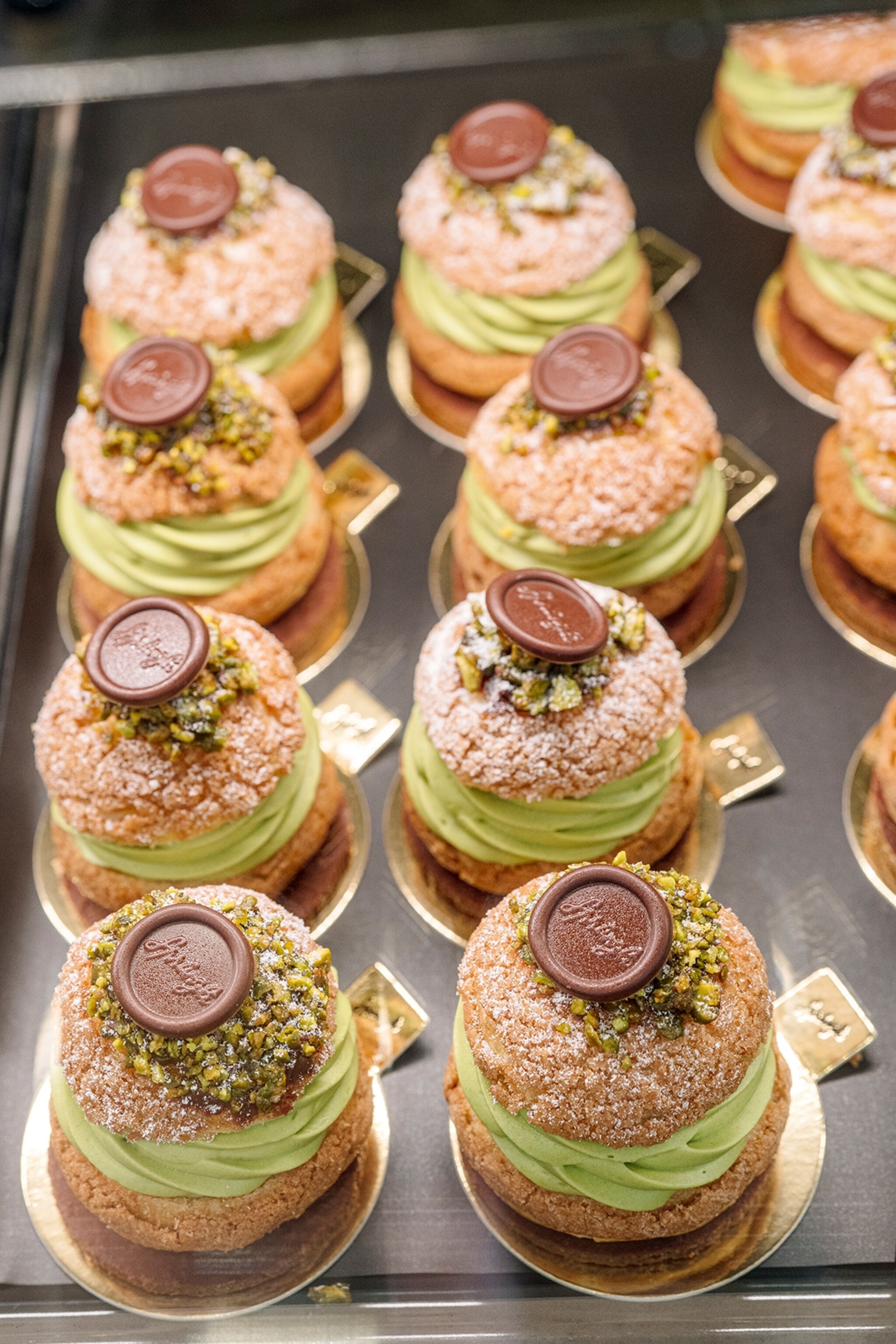A close-up shot of neatly lined-up choux buns on gold paper discs, filled with a pistachio cream.