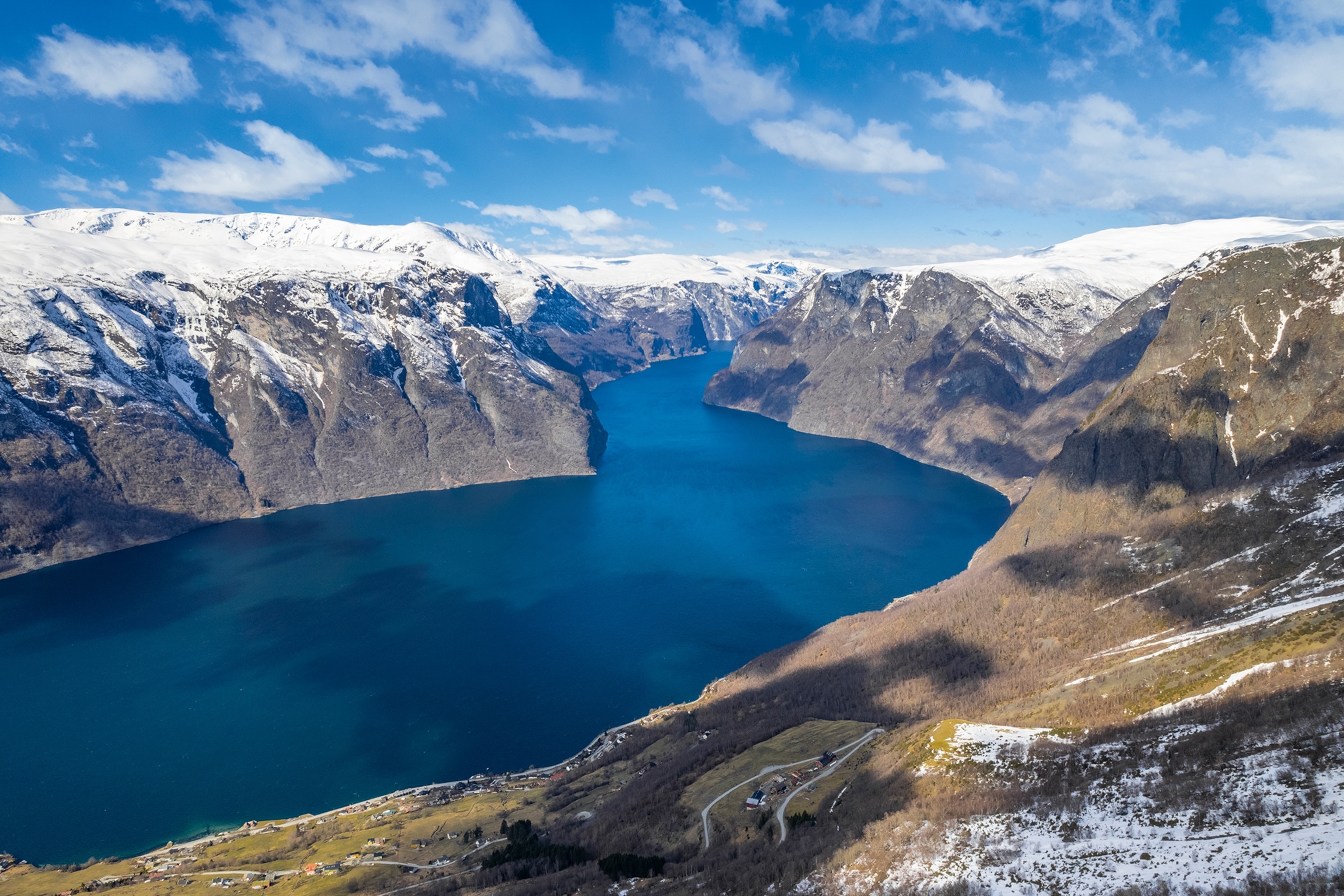 A mountain viewpoint overlooking a wide river valley with a snow-tipped mountain range in the distance.