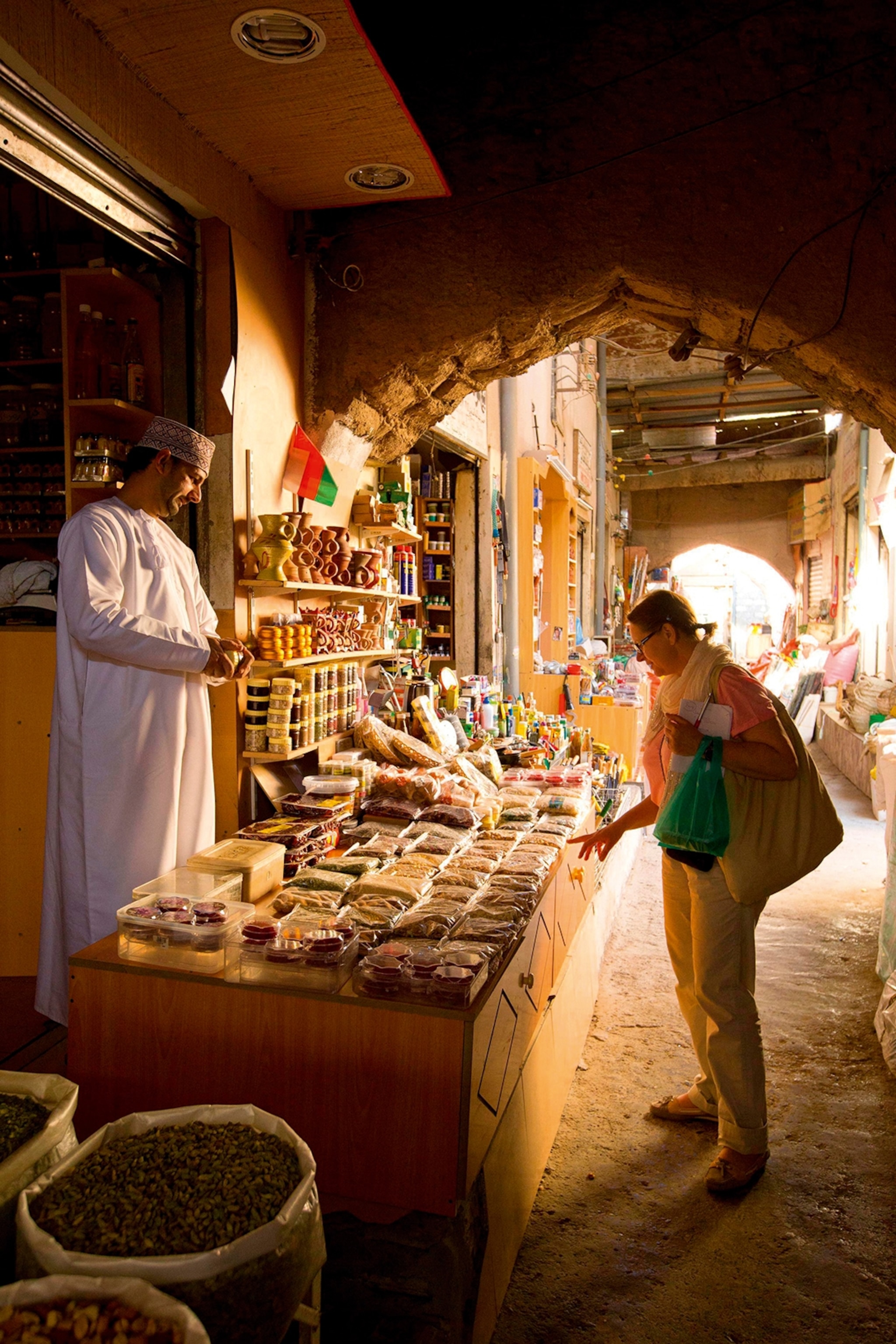 A spice stand in a souk in Oman with a visitor selecting spices to buy.