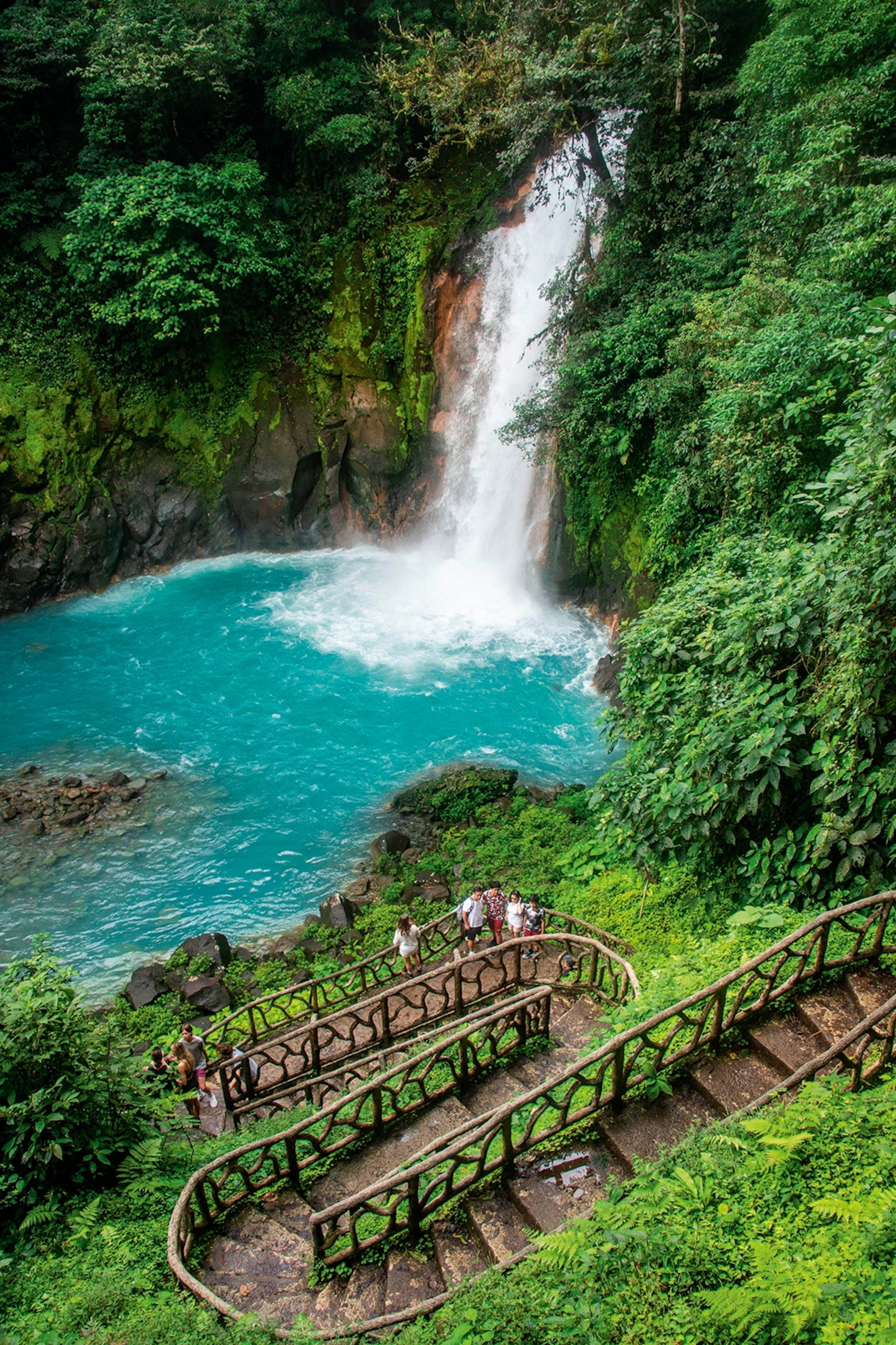 A tall waterfall cascading from a cliff into a turquoise pool of water surrounded by a rainforest.