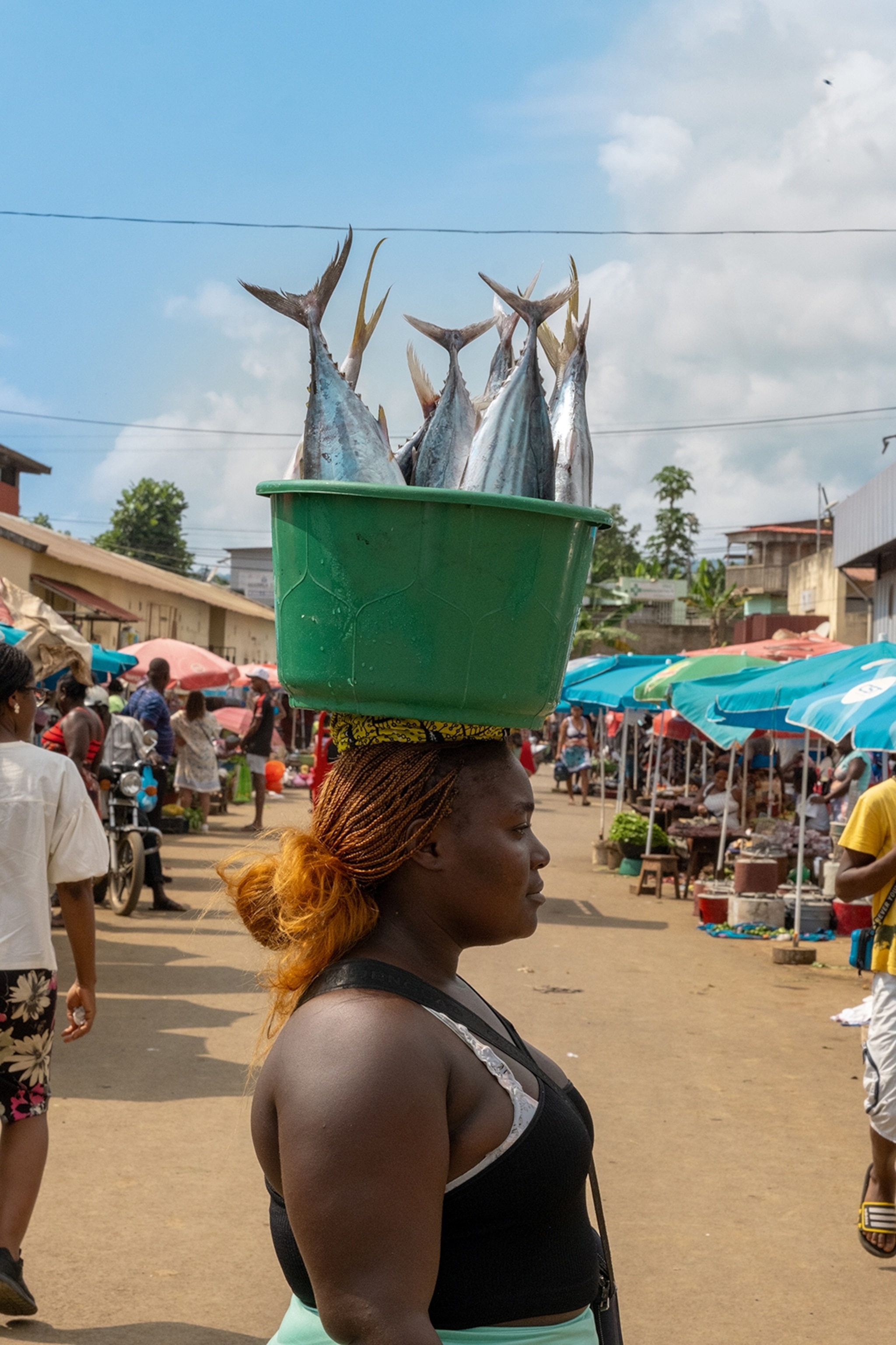 A local woman at a market, carrying a bucket with fish - fins pointing at the clear sky.