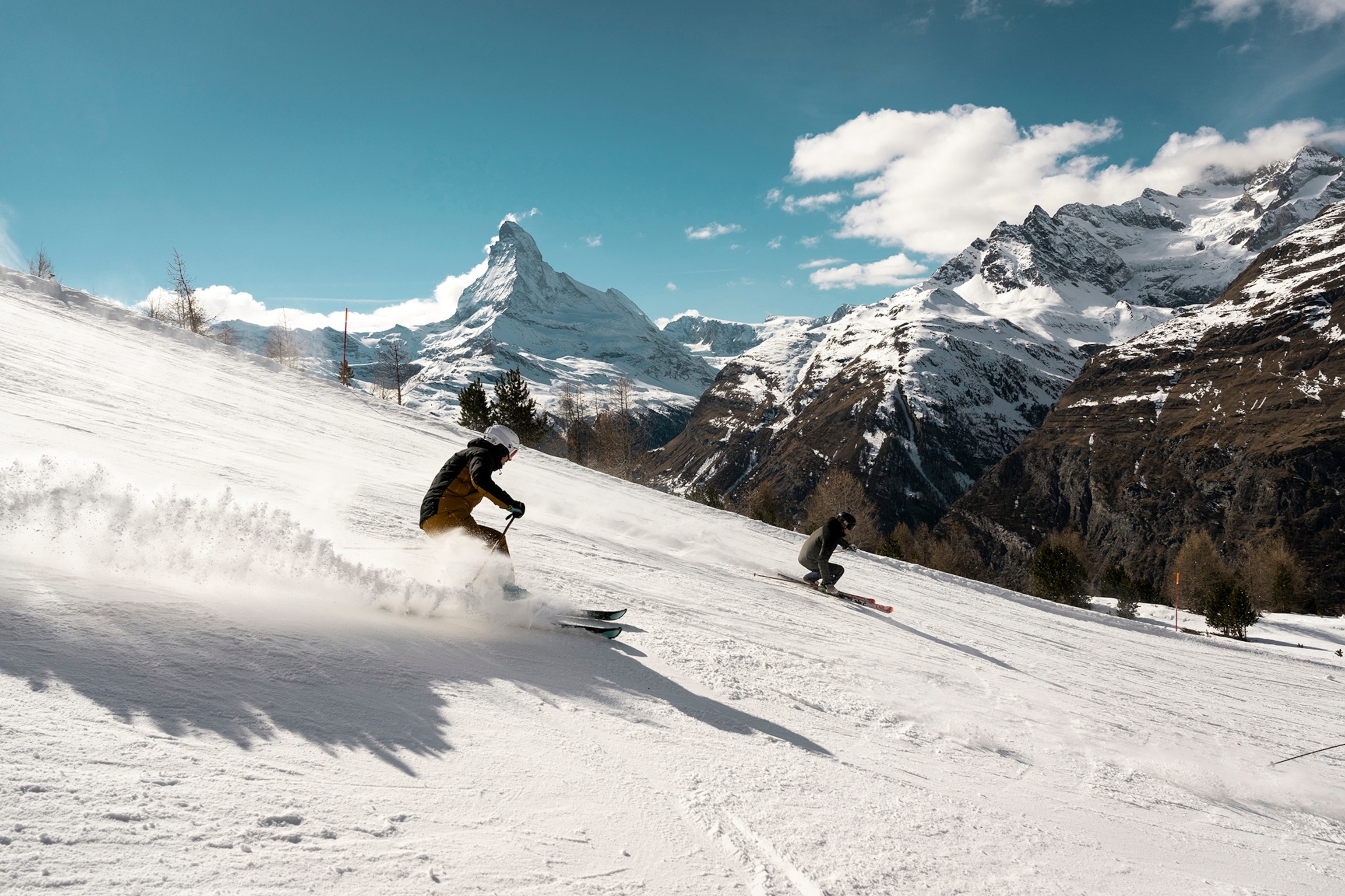 Two skiers dramatically going down a slope, whirling up snow.