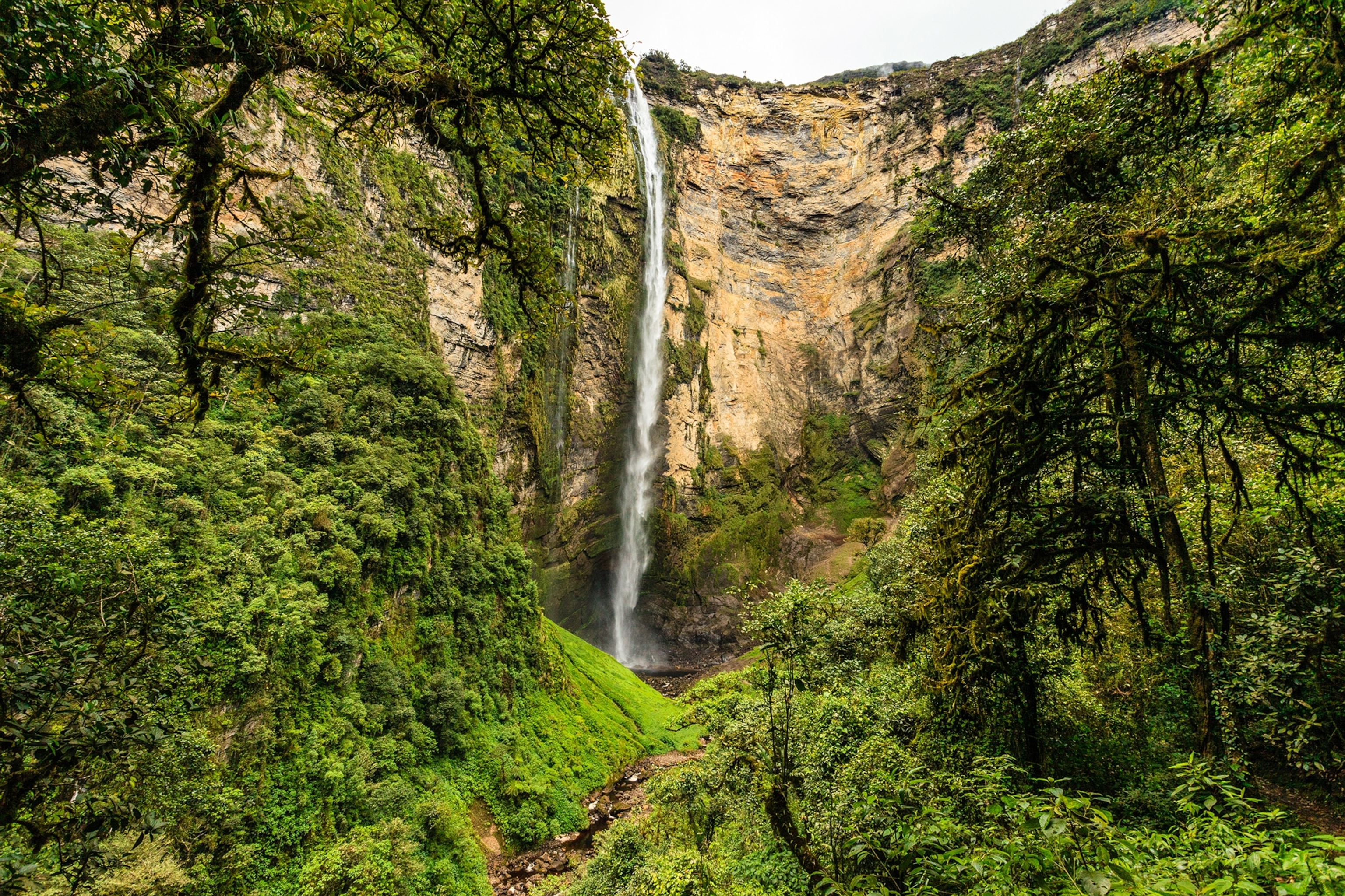 Waterfall plummeting from a mountain top with lush greenery covering the mountainside