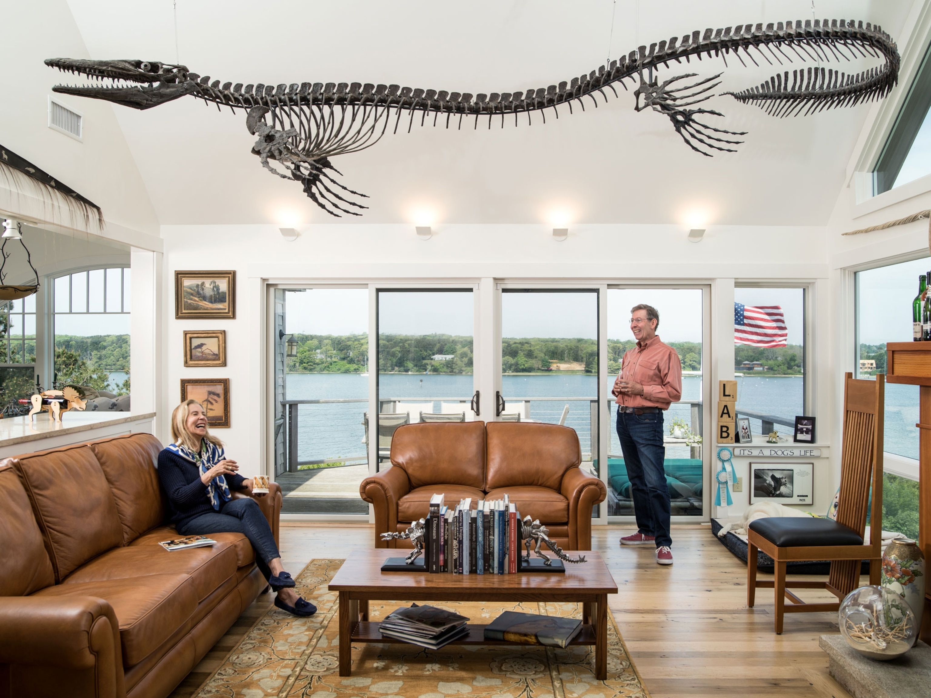 smiling man and women in large waterfront room with dinosaur suspended from ceiling.