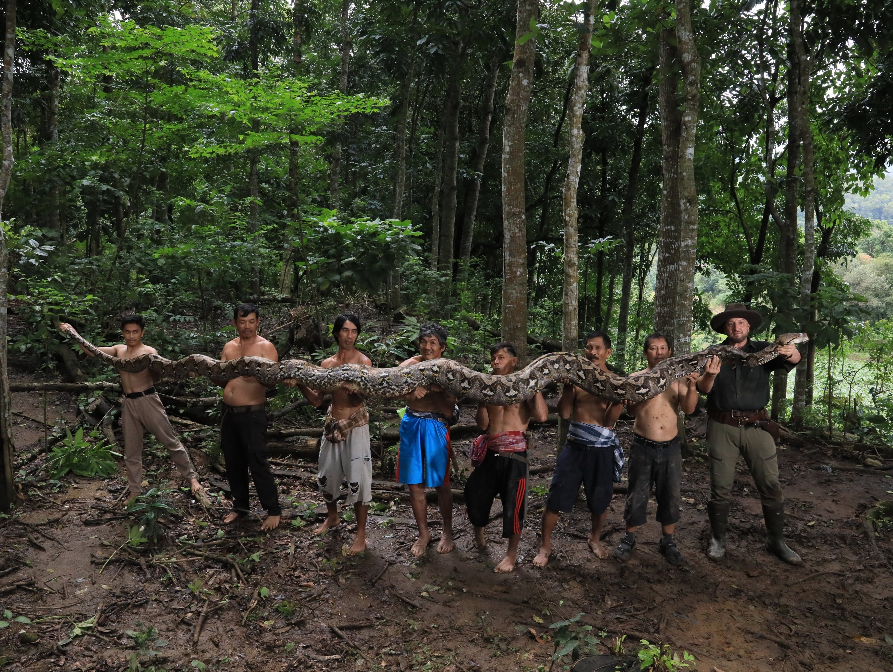 A group of men stand in a line holding the long body of a snake.
