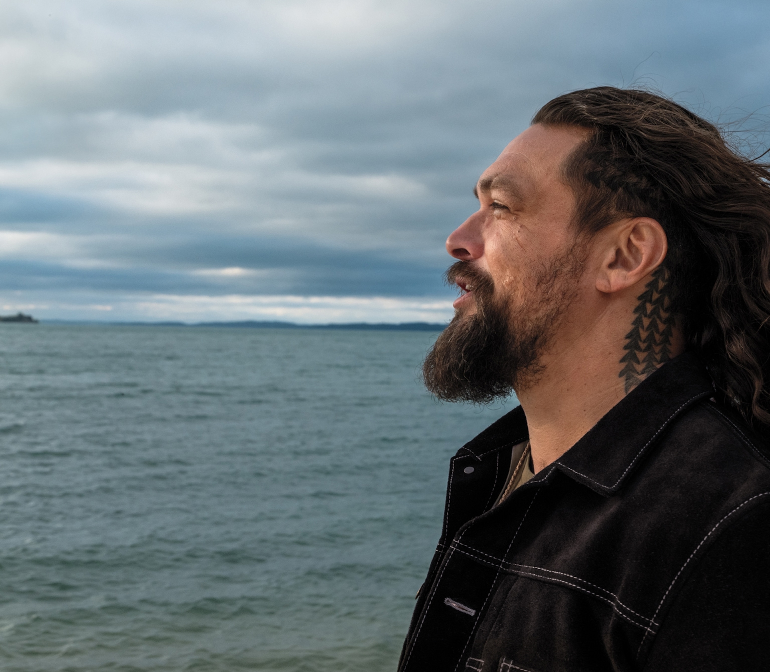 A man stands horizontally to the camera overlooking a body of water.