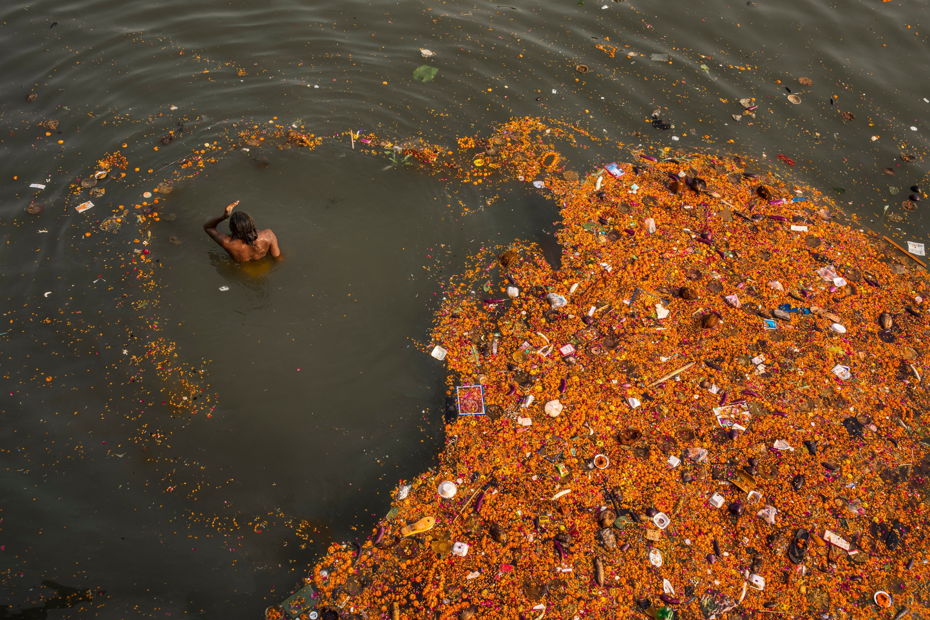 Plastics and other pollution mix with offerings of flowers in the sacred Ganges River in Varanasi (Binaris), India.