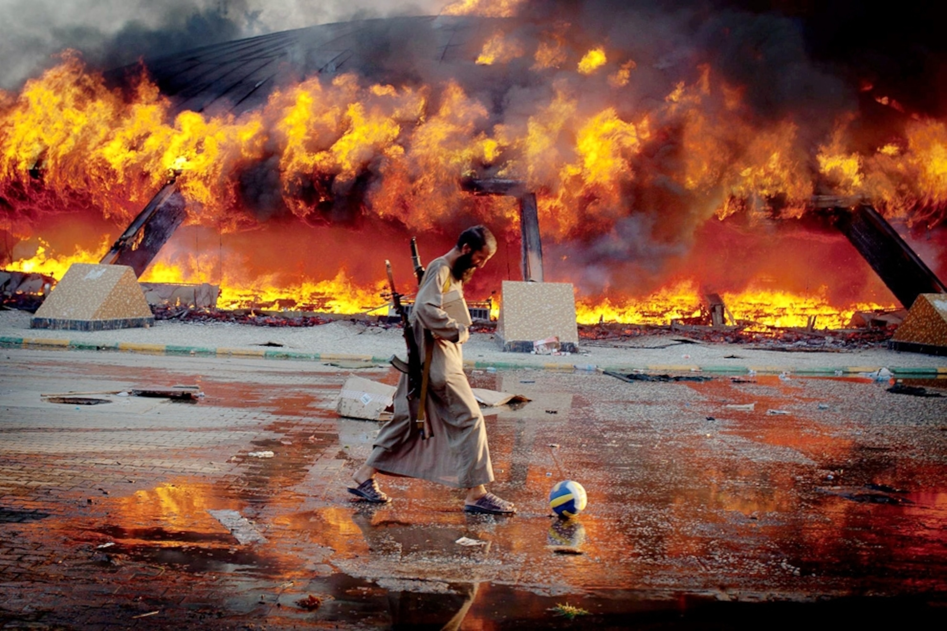 Libya picture: man kicking a soccer ball near Qaddafi's burning compound -- for best pictures of August photo gallery