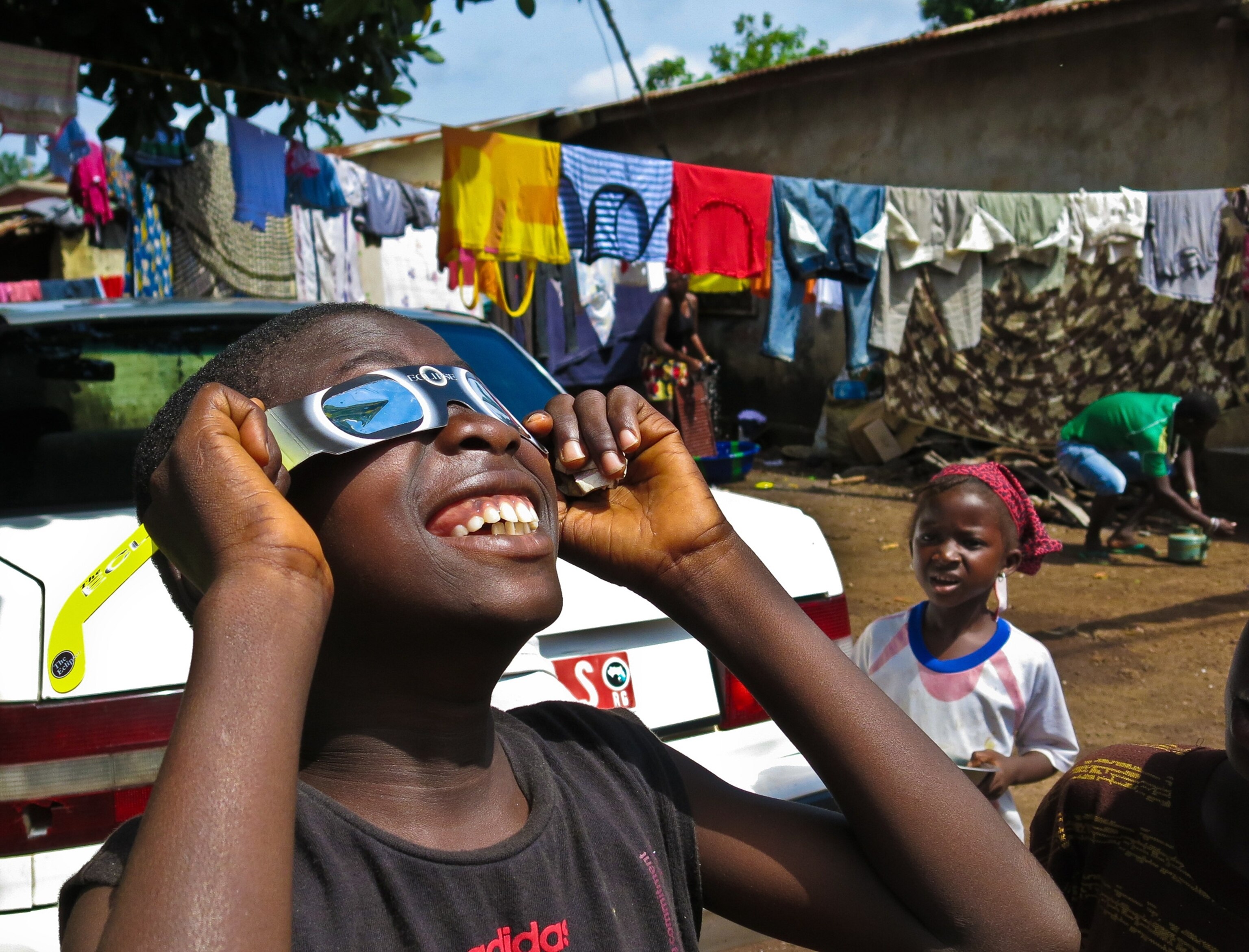 a young boy grinning as he looks through glasses to view a solar eclipse