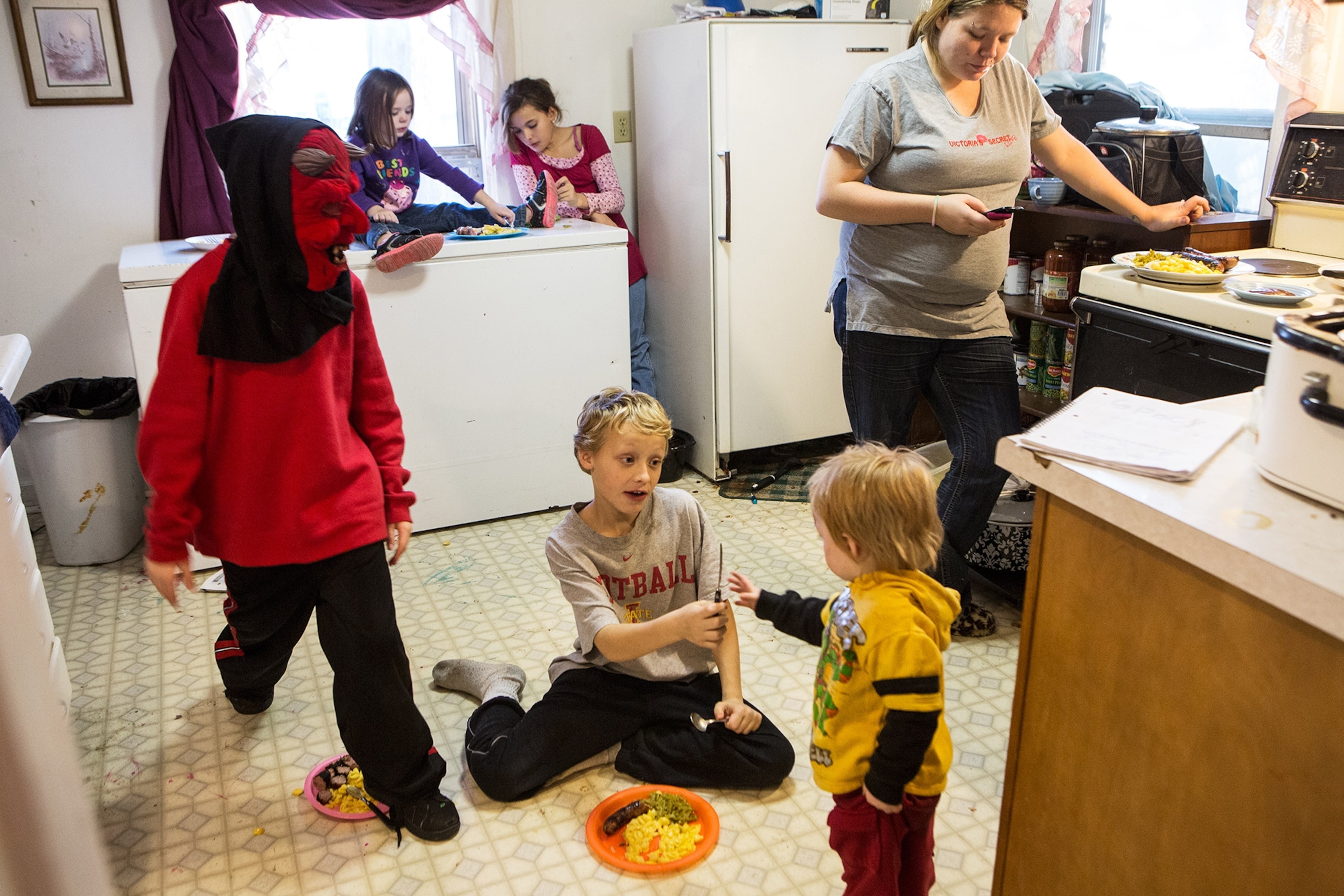 children sitting on the floor of a kitchen eating a meal