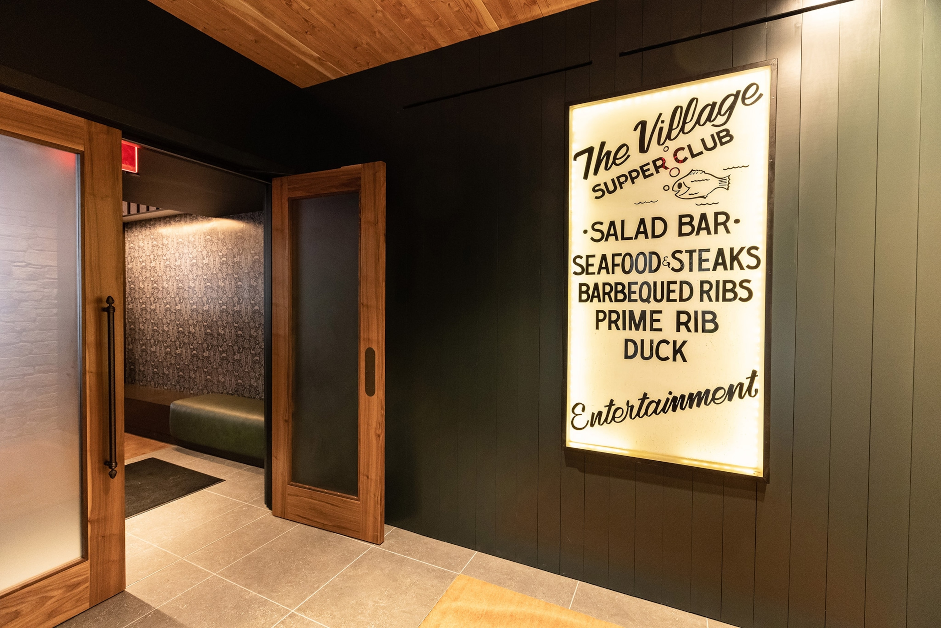 An interior of a restaurant entrance with a sign reading "Village Supper Club" with a list of food offerings, a door stands open
