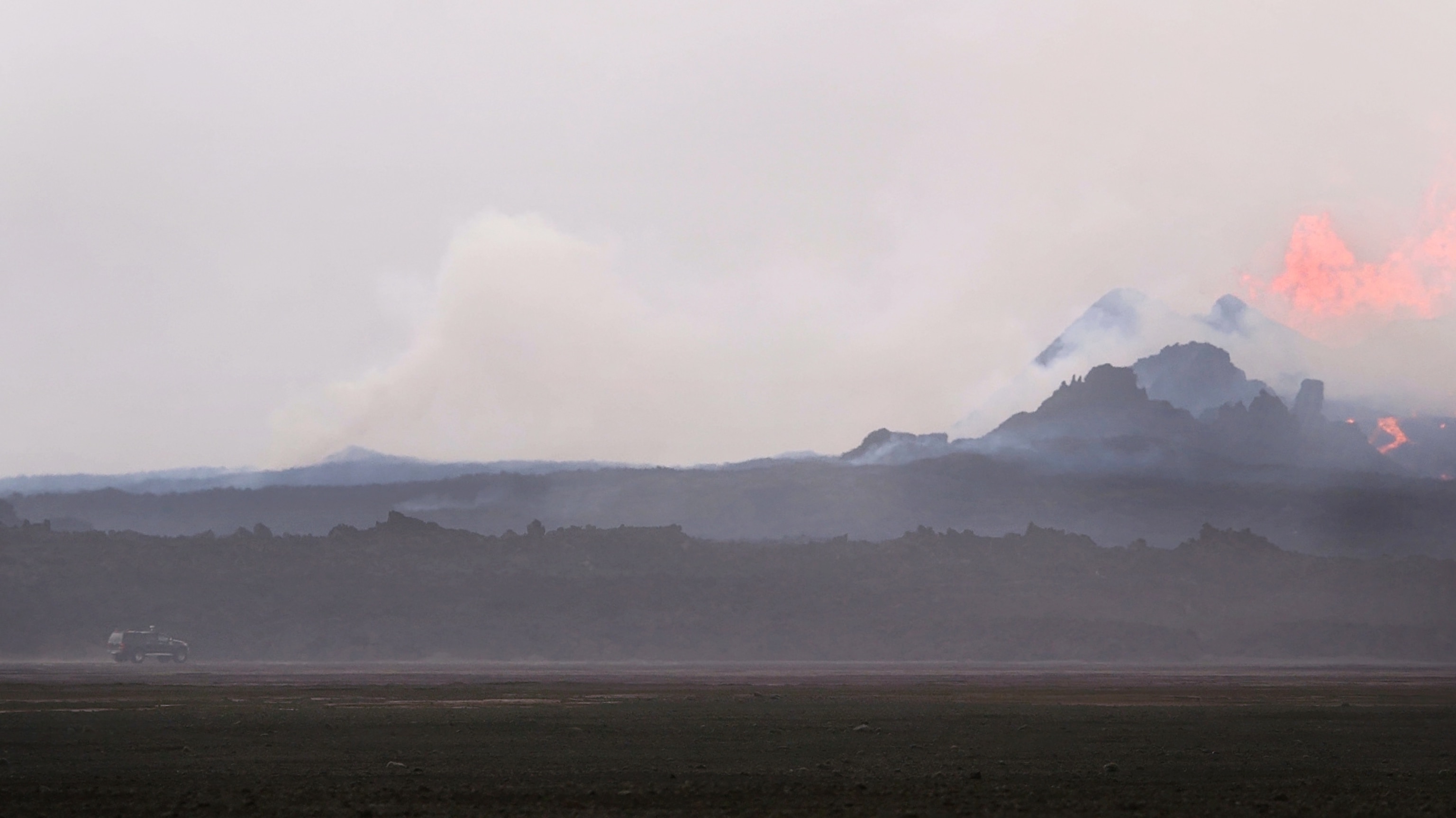 A four-wheel drive vehicle drives toward the erupting fissure, showing the scale of the eruption