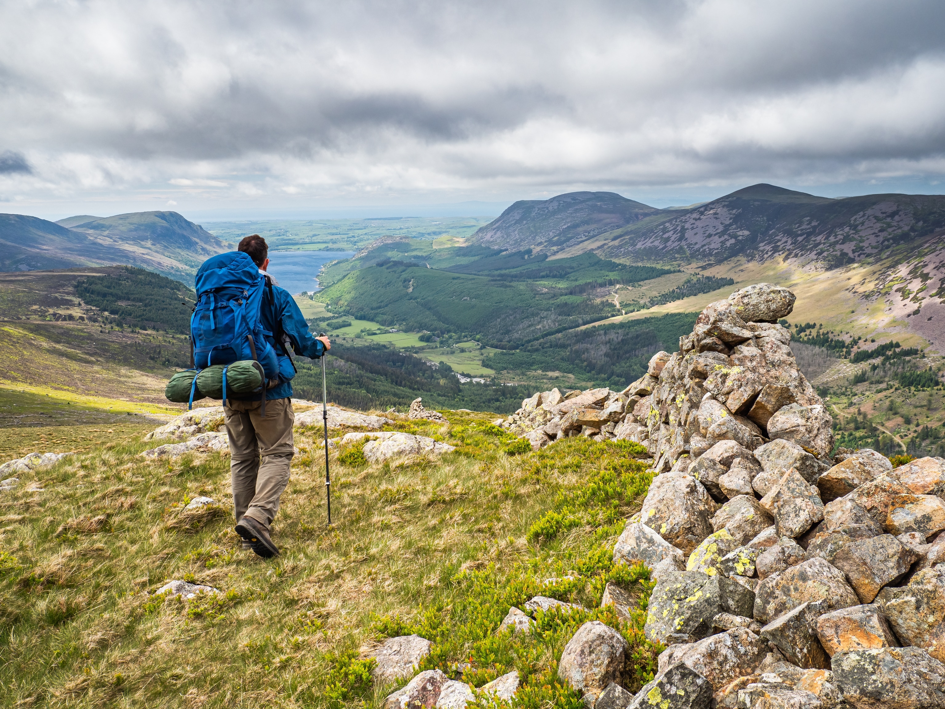 A drystone wall stretches towards distant Buttermere on Warnscale with a hiker heading towards the mountains.