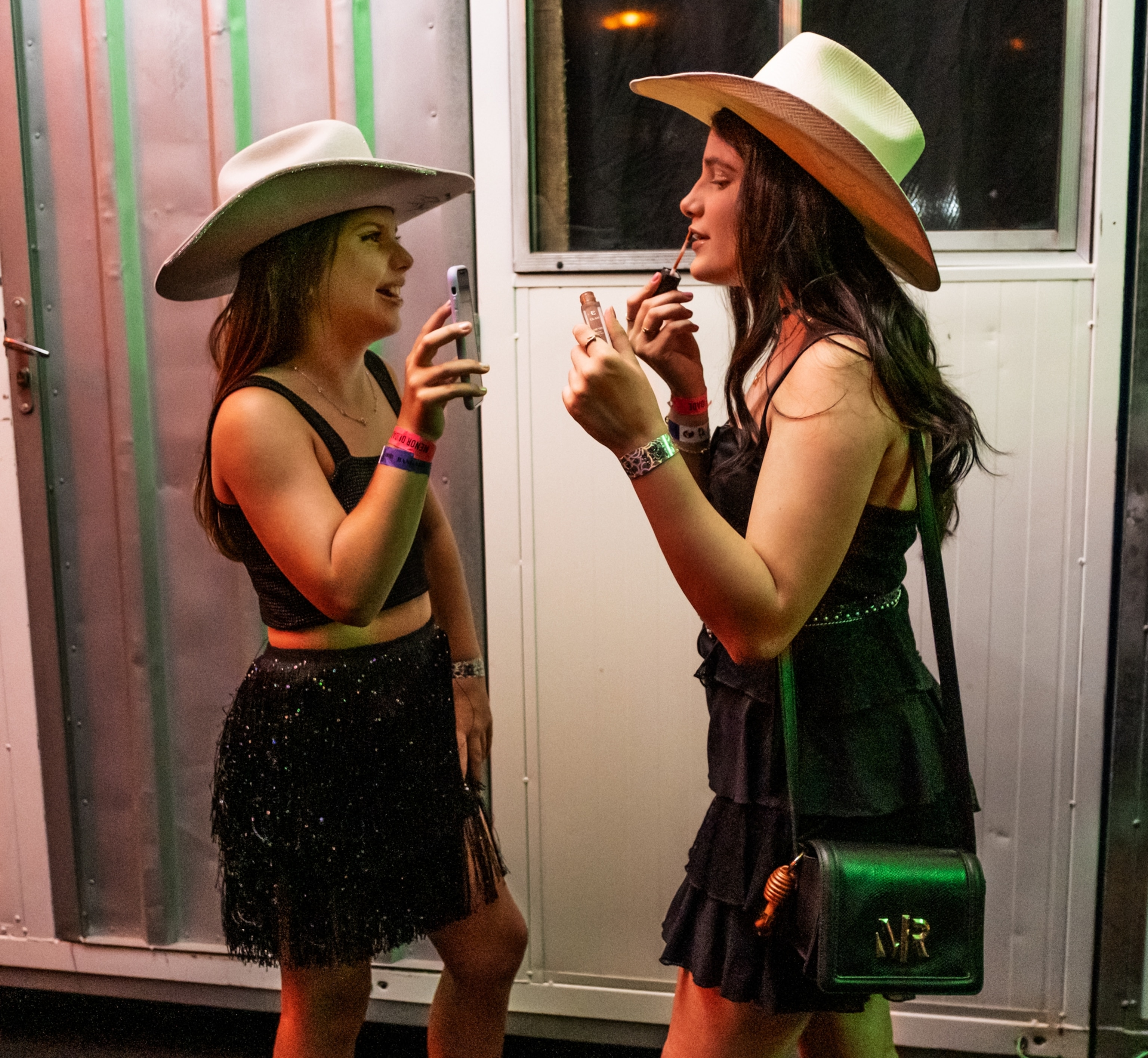 Melissa Lopes Nogueira (at left) hold the phone up for Júlia Arana Silva to use as a mirror as she applies lipgloss.