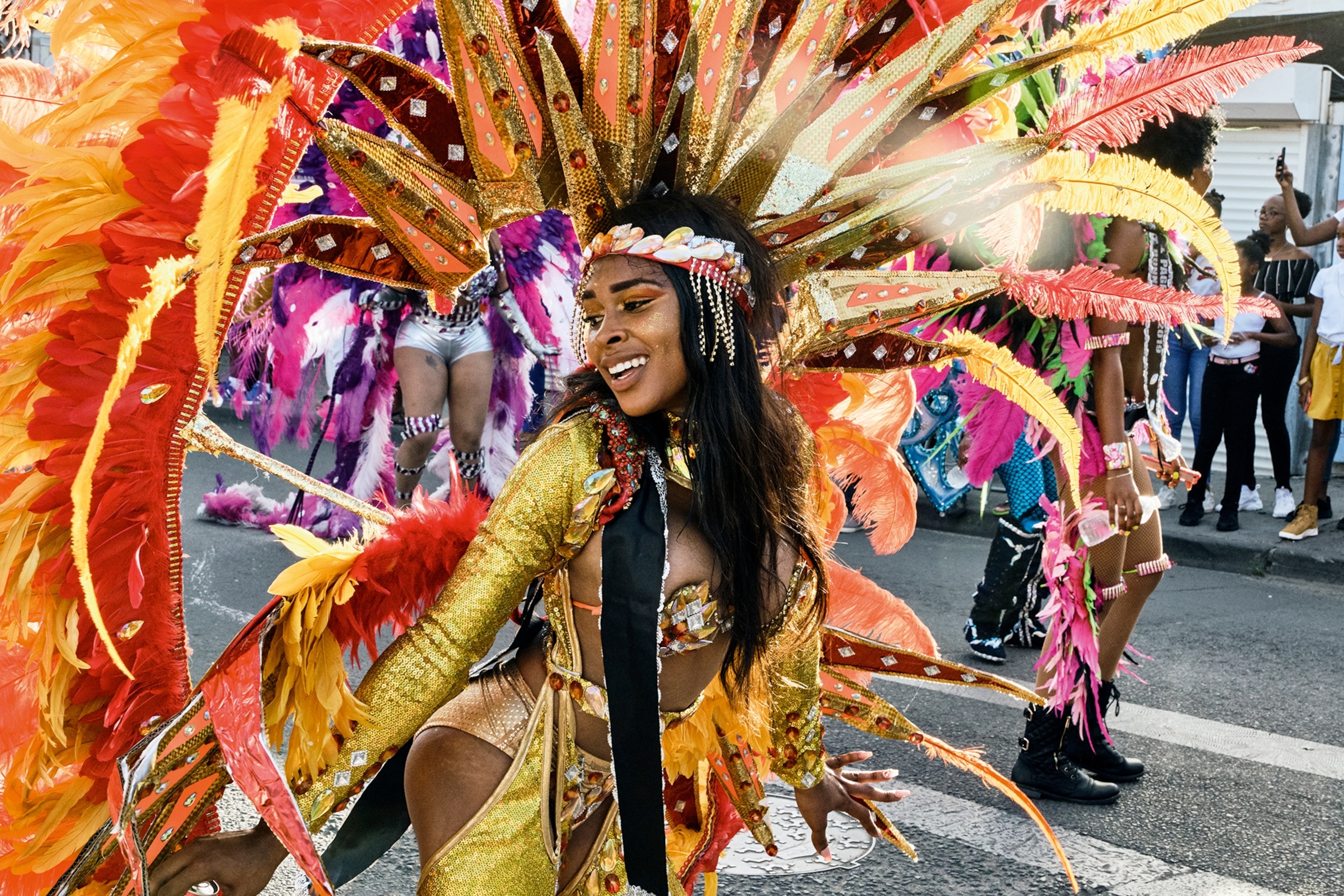 A dynamic close-up of a woman in glittery and revealing costume, smiling and wearing a feather-like headpiece.