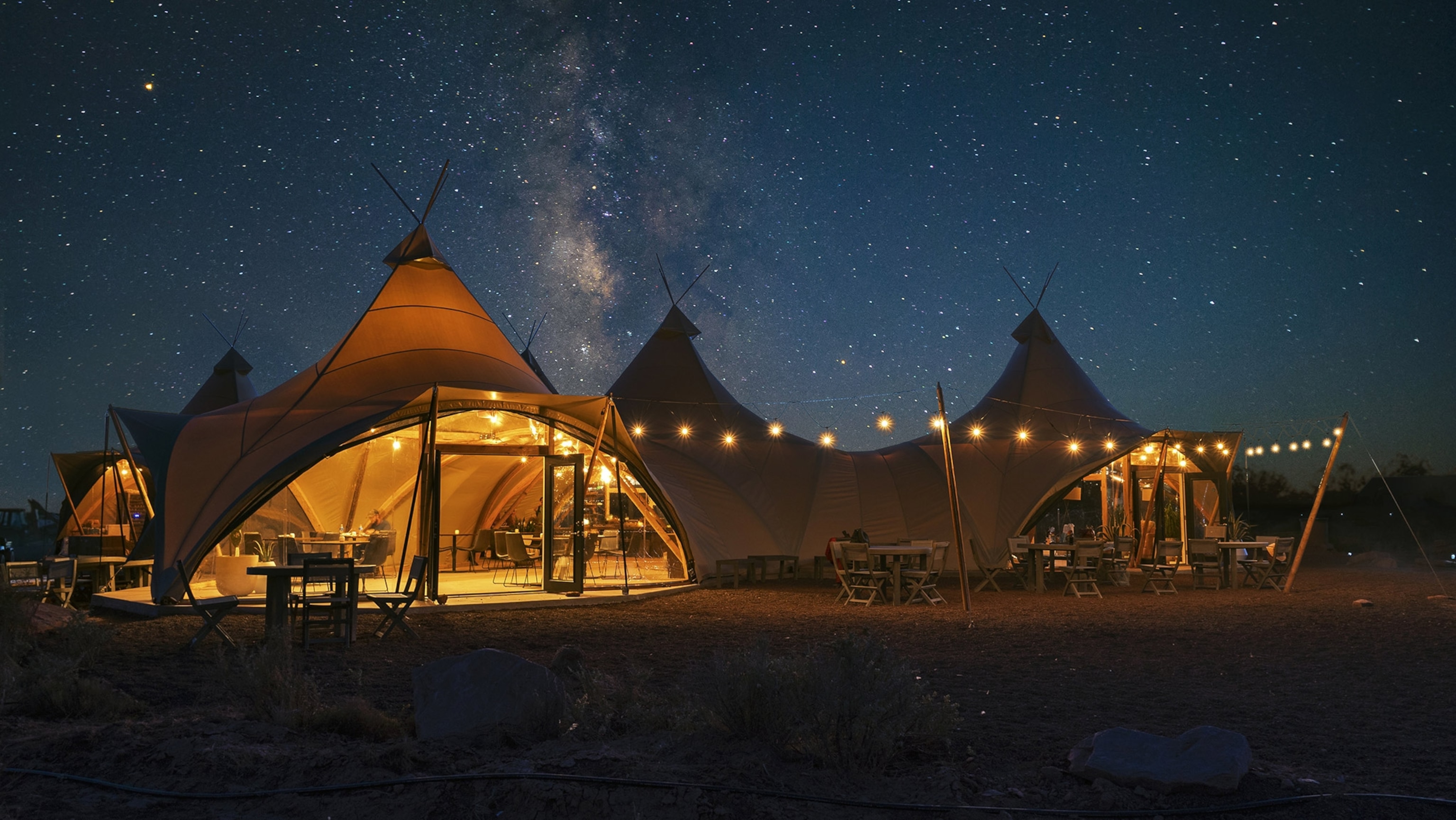 A cluster of tents warmly lit stands against a starry sky