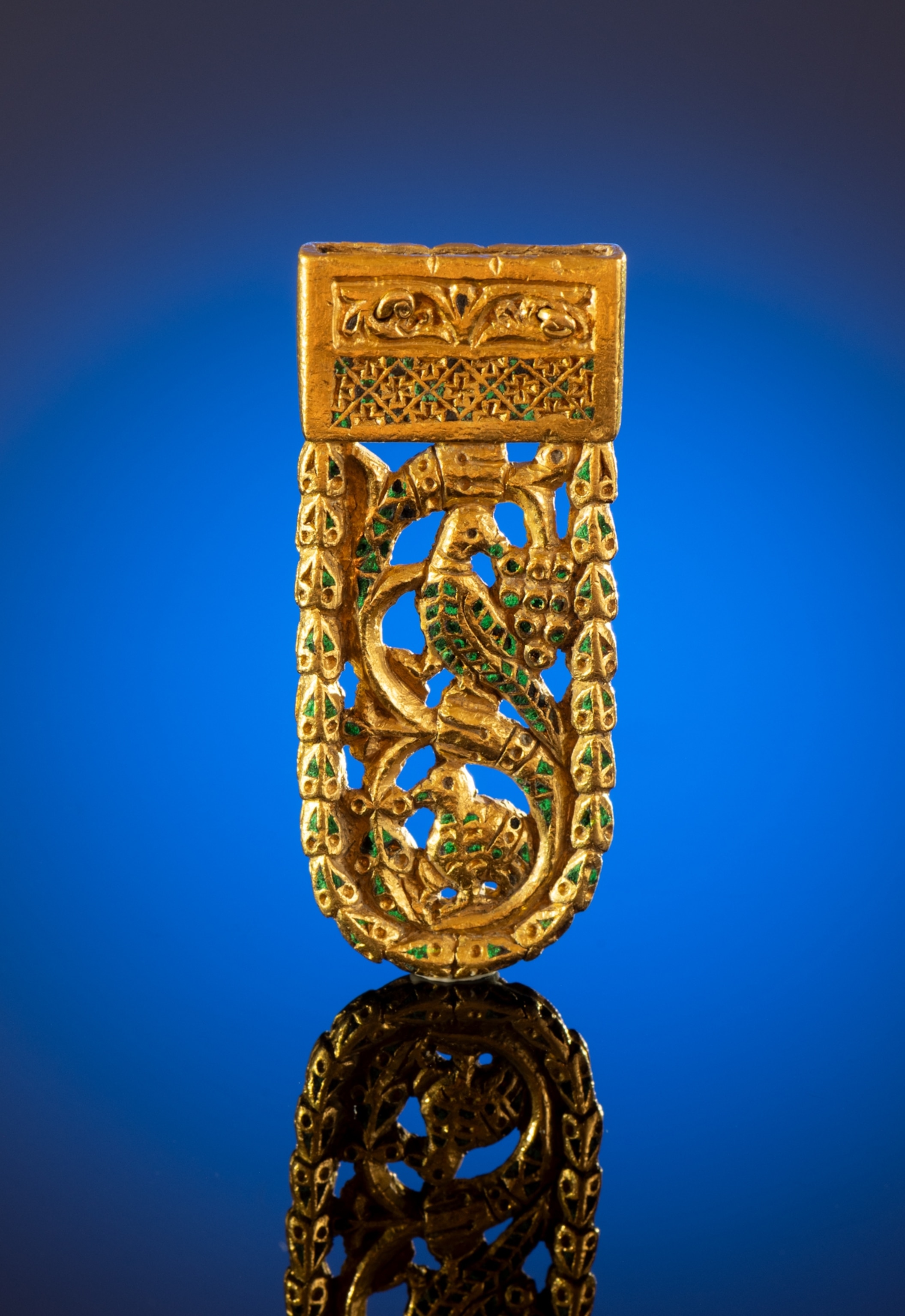 Intricate shiny, gold belt strap showing two birds stacked vertically with various geometric patterns and green gemstones surrounding them to create an arched shape.