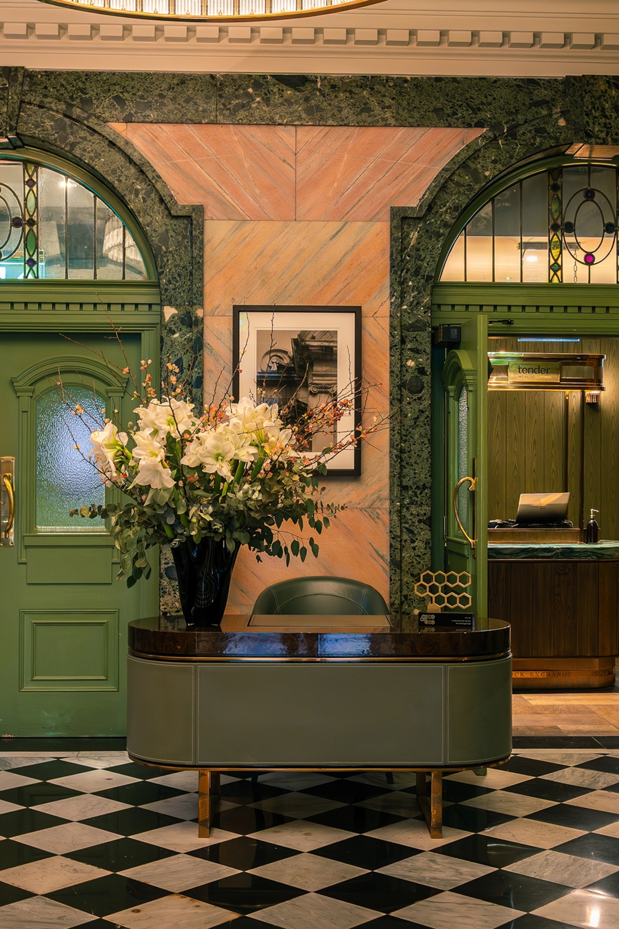 A luxurious hotel lobby with painted, arched doors, a marble tiled floor and a big bouquet on the reception desk.