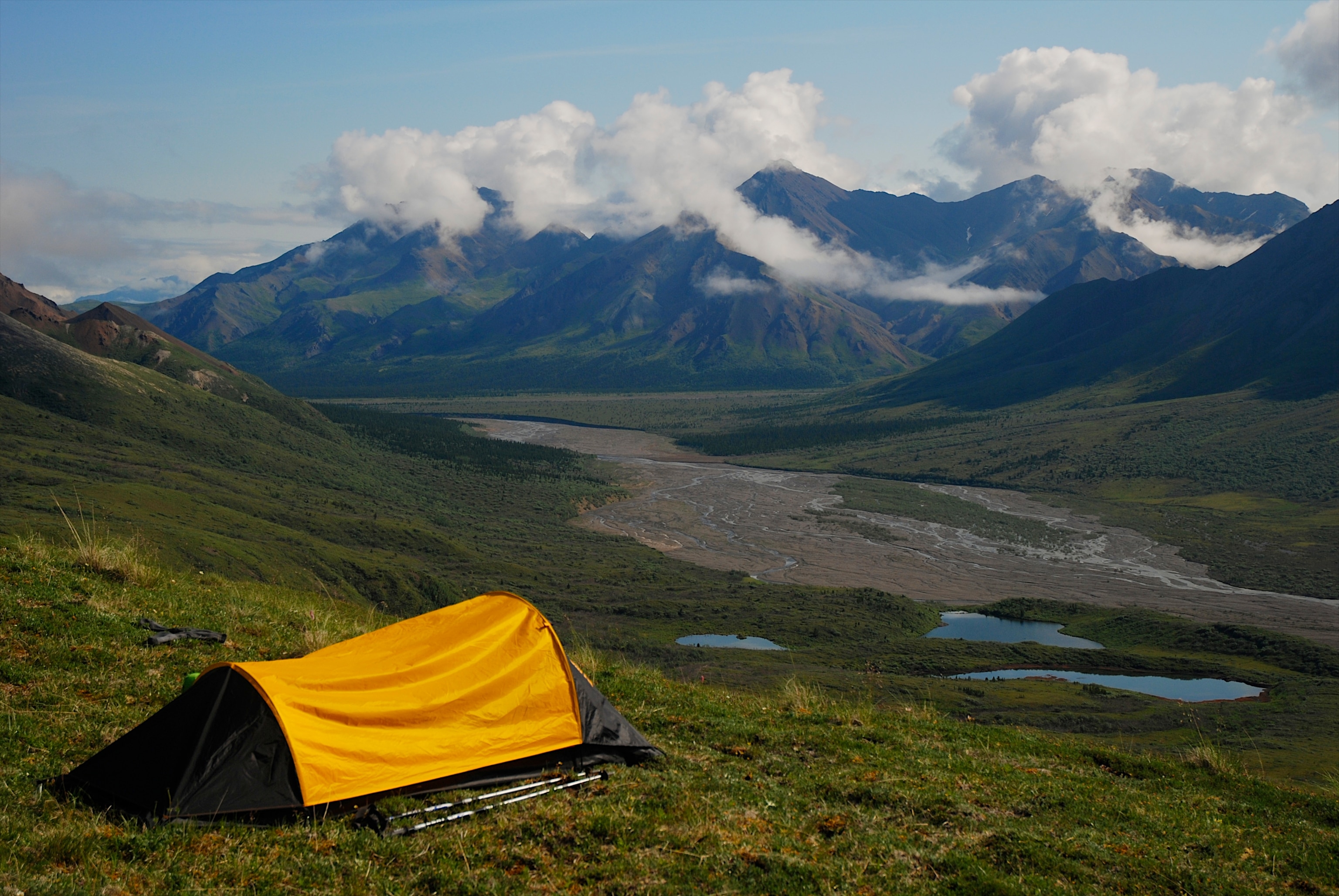 An orange tent is set up on a large hill in Denali National Park with snow covered mountains in the background