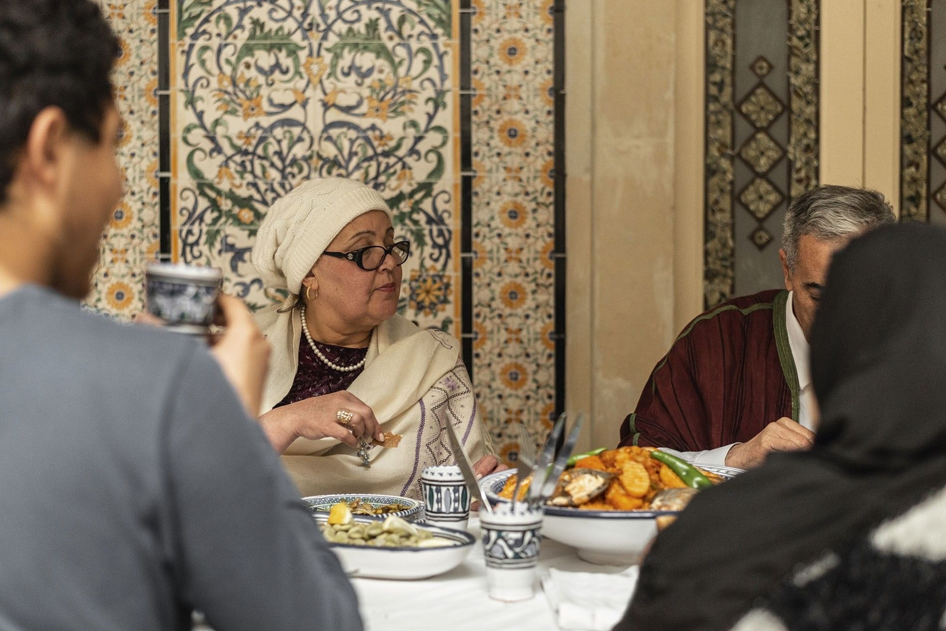 The family gathers around the table laden with dishes showing off a plethora of colours.