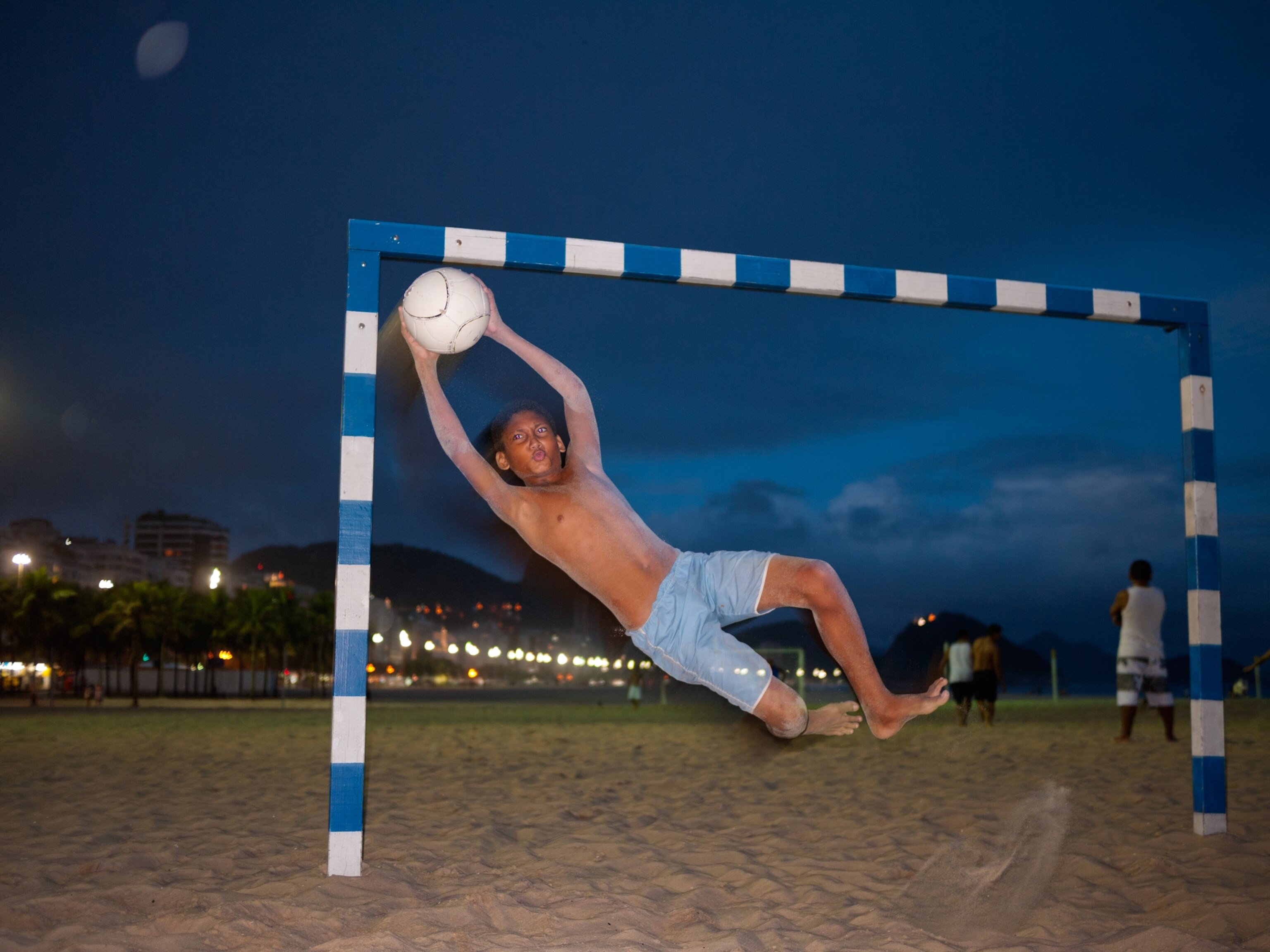 a goalkeeper catching a soccer ball on a Rio beach