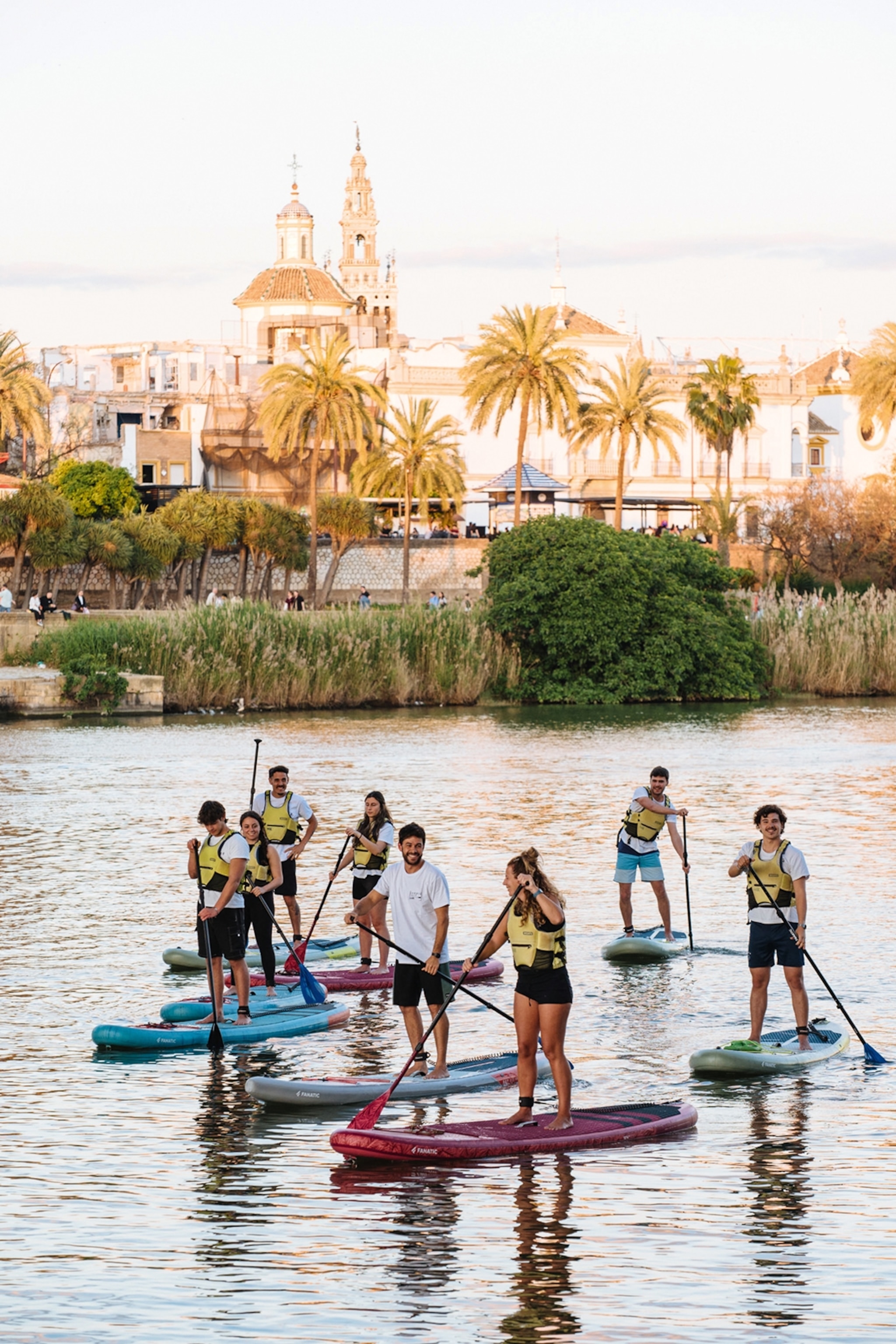A group of young people wearing life jackets on individual paddle boards, going down a river.