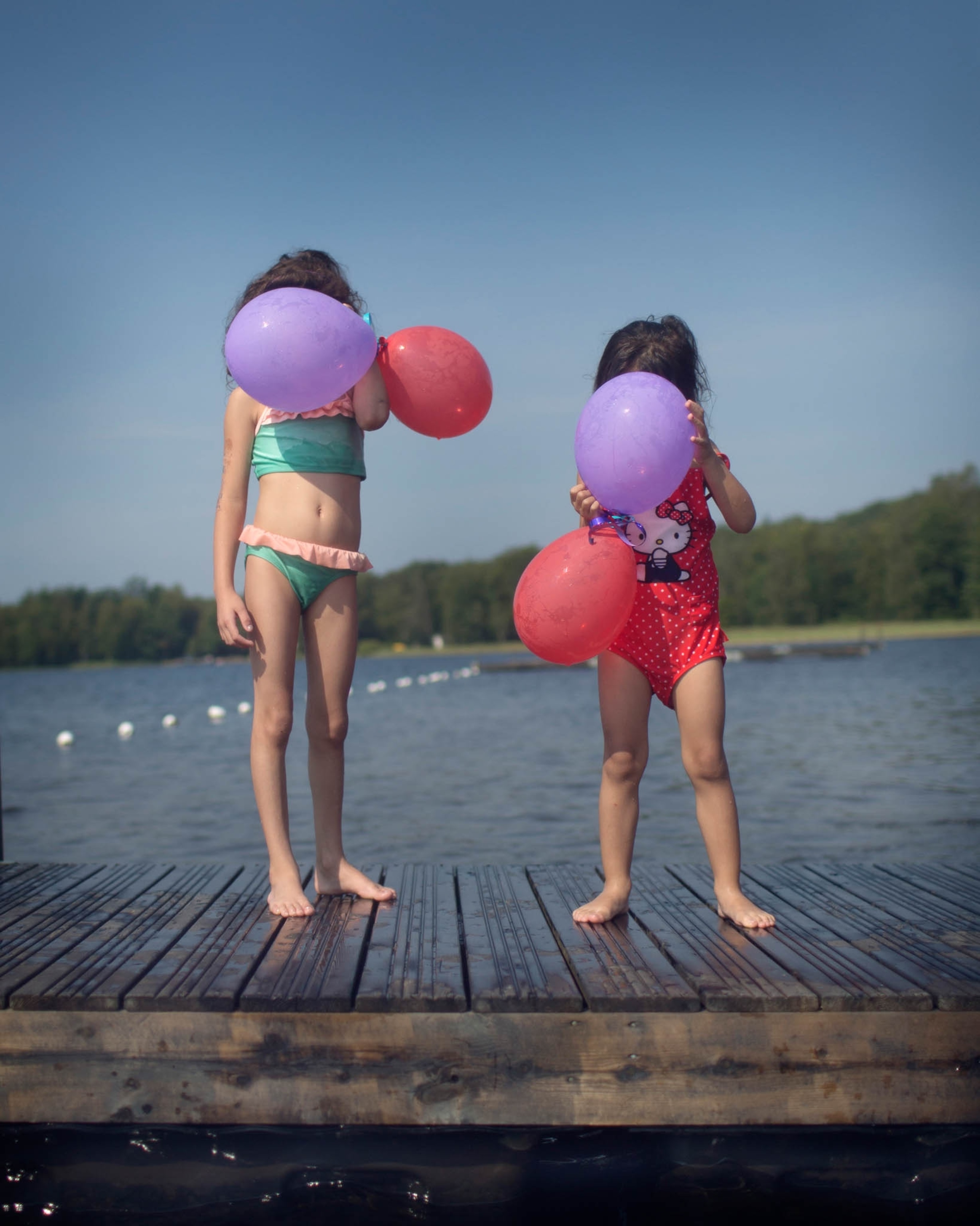 two girls in swimsuits holding balloons on their faces