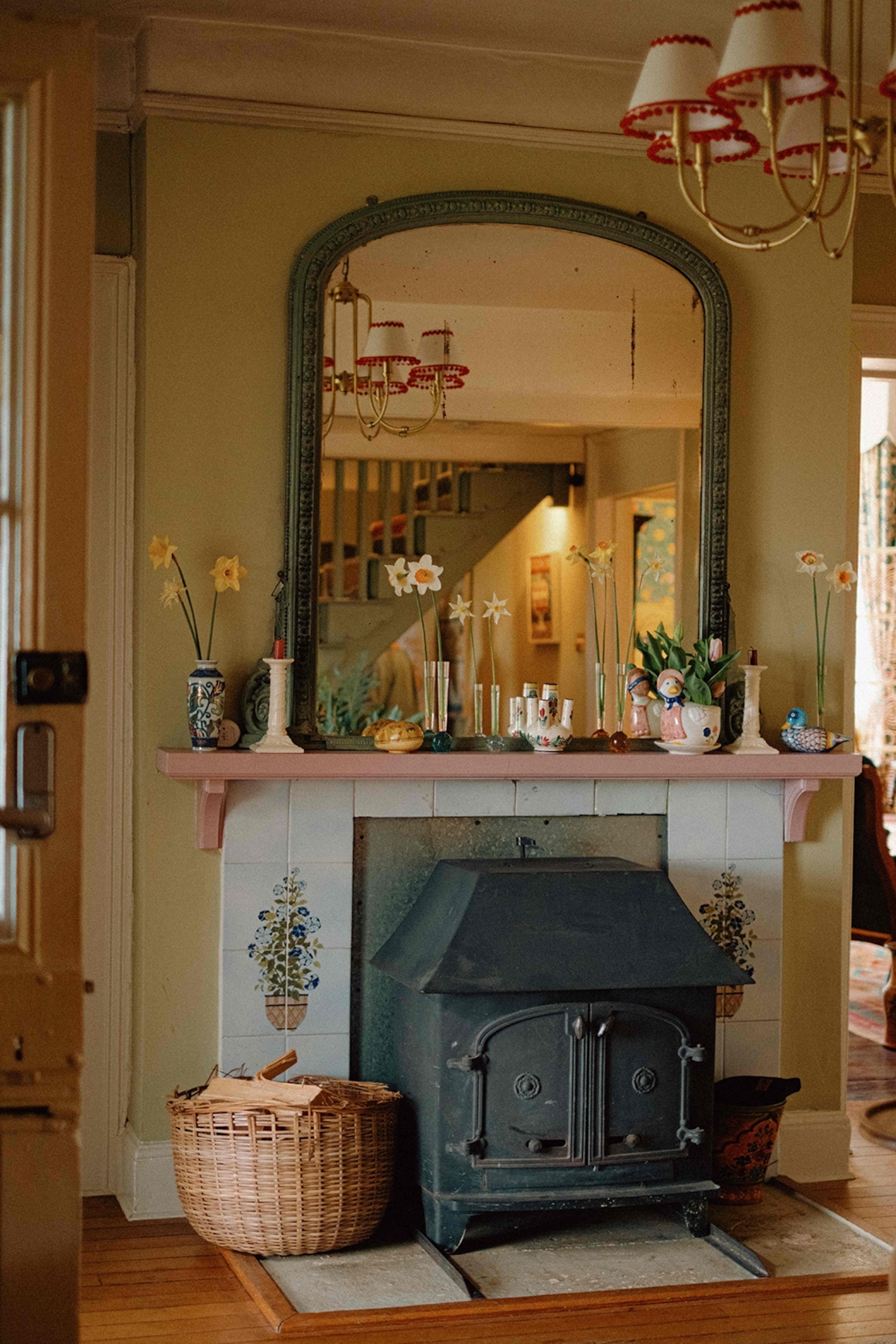 A decorated farmhouse fireplace with daffodils on the mantelpiece and a vintage mirror hung above.