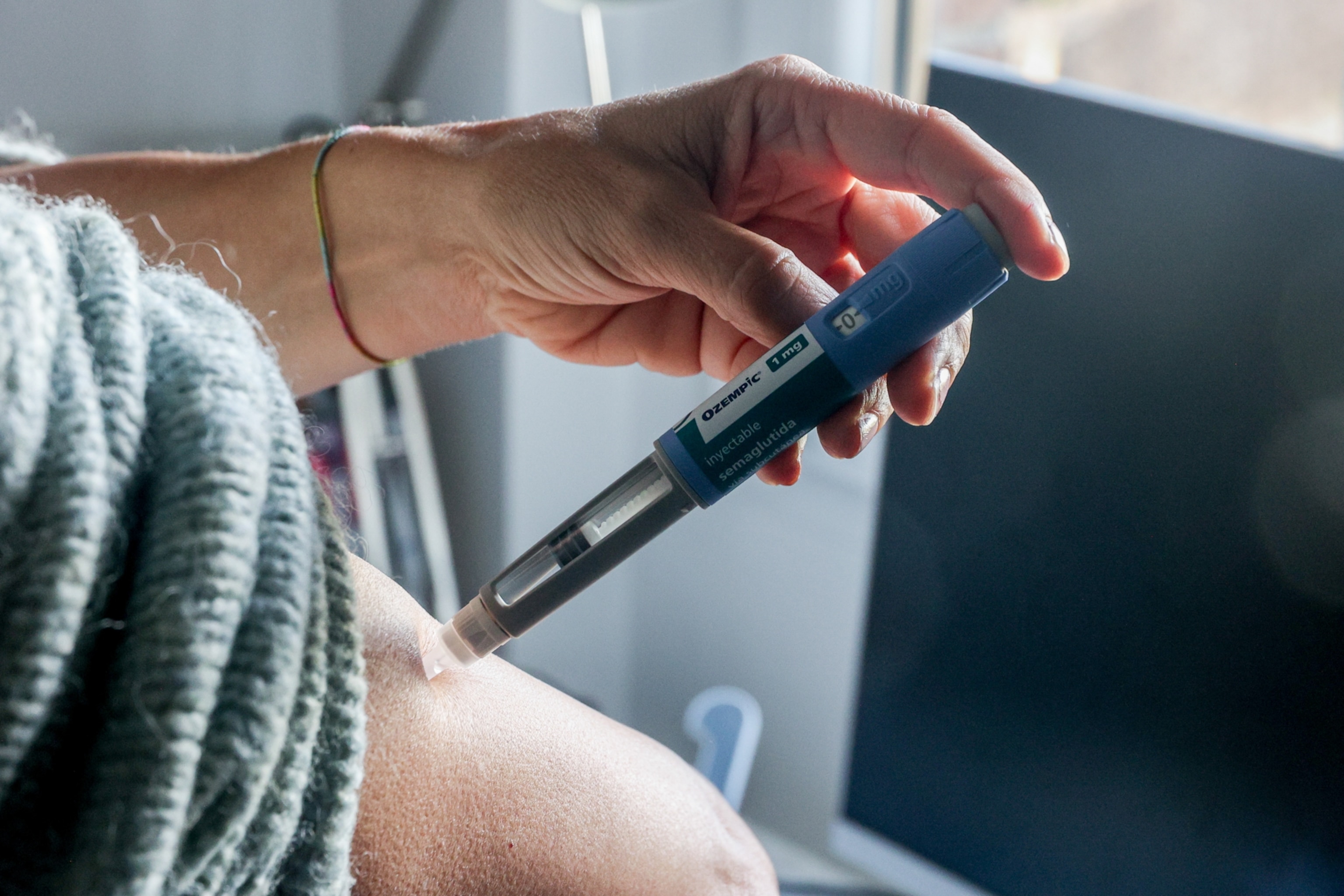 A person using one hand to inject their abdomen using a blue Ozempic multi-dose syringe.