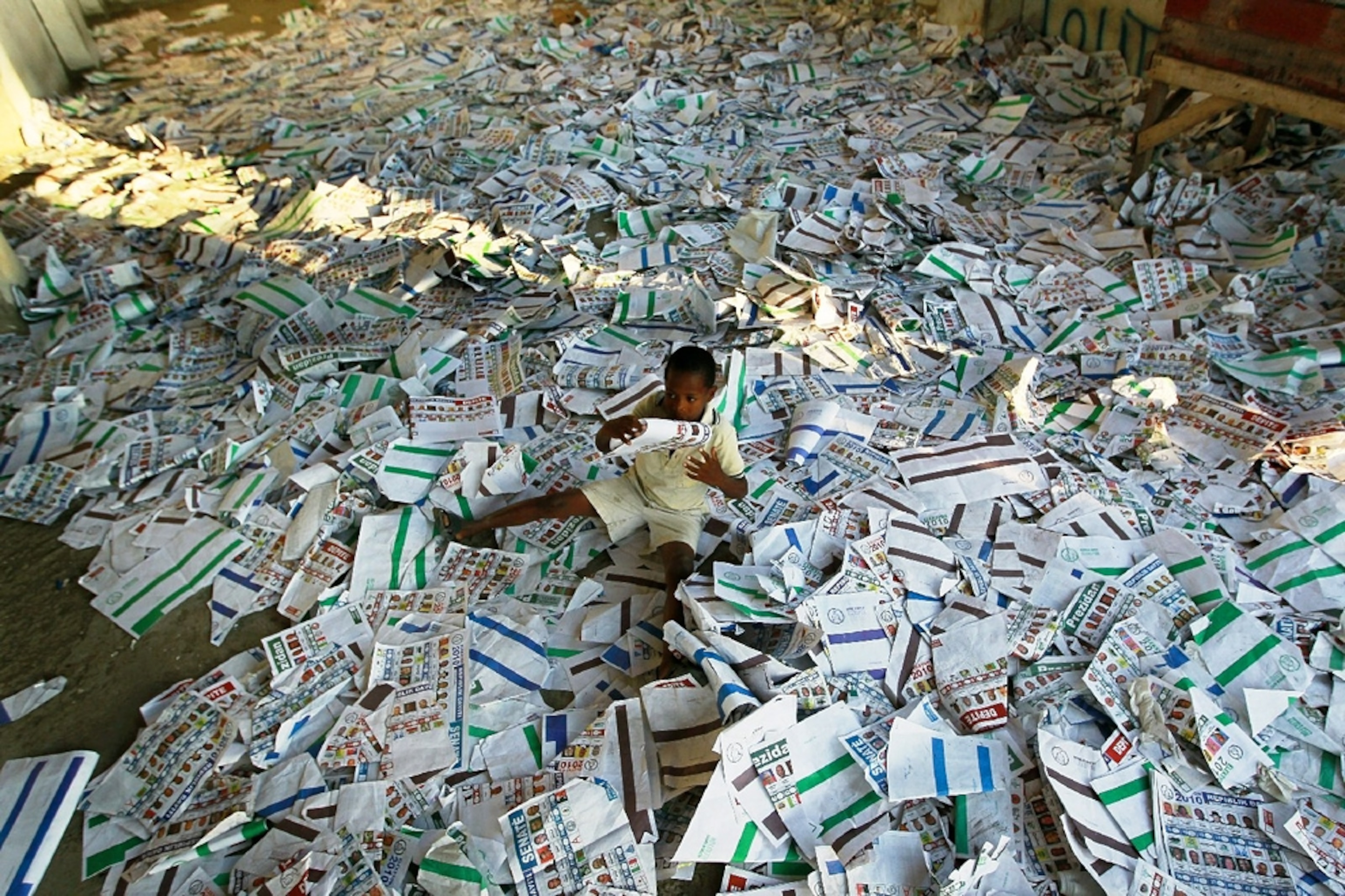 A child sprawls across a room-sized pile of ballots for a Haiti election -- picture from a photo gallery on the one-year Haiti-earthquake anniversary