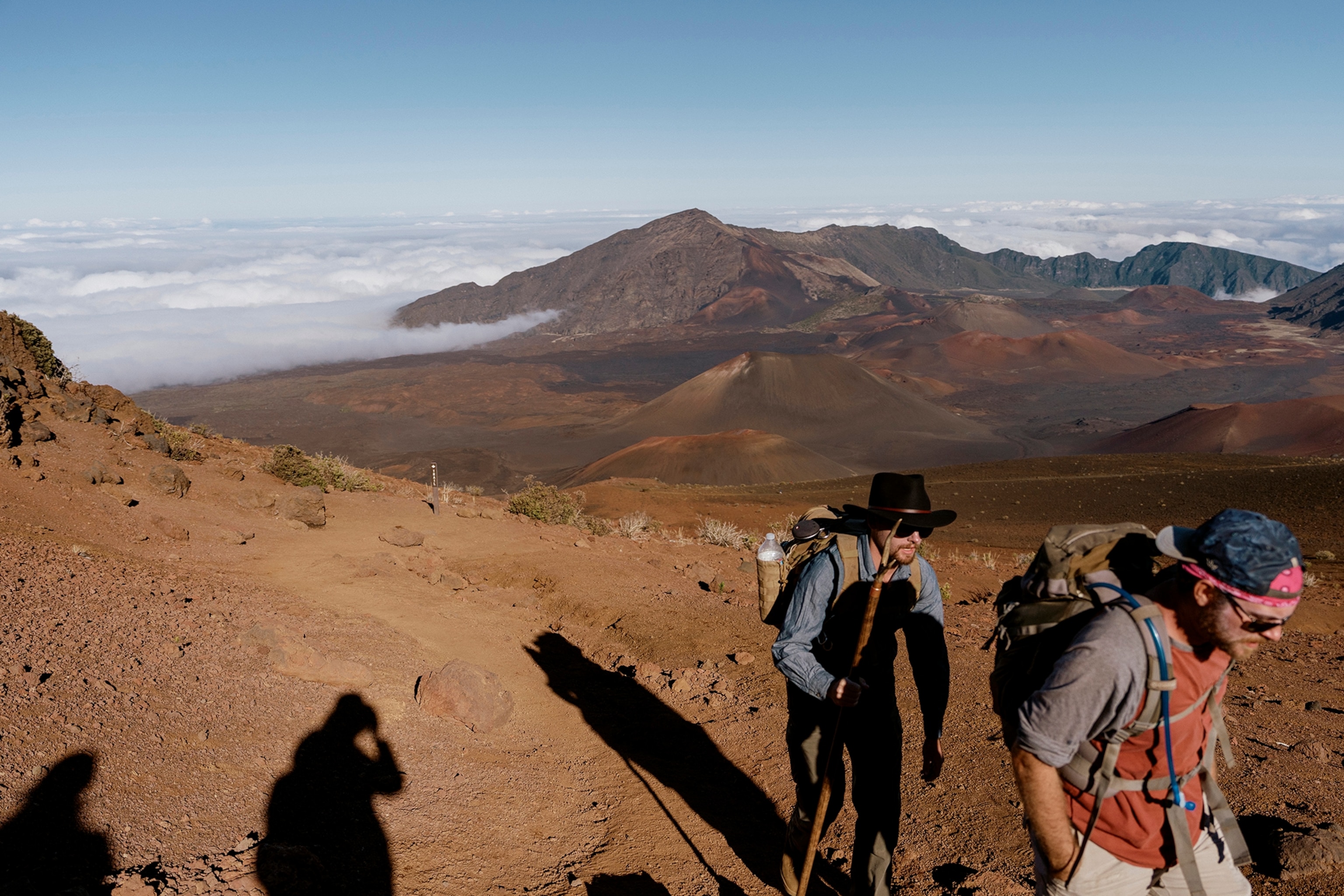 Maui, HI- December 16, 2023. Two hikers near the summit of Haleakala, with the crater in the background. Haleakala is an active shield volcano that is 10,023 ft tall.