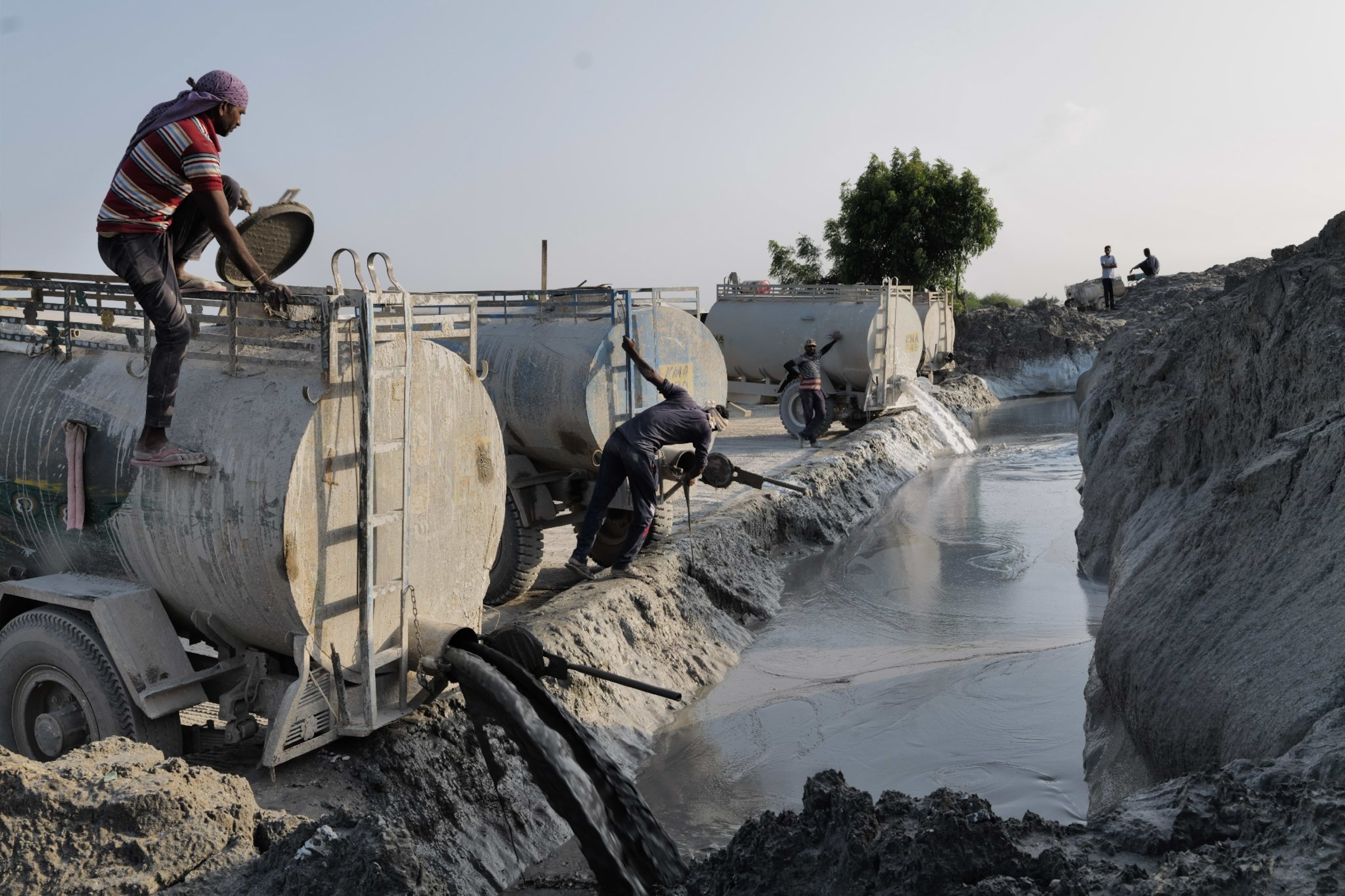 Men working at the dumping one is standing on top of the truck as slurry pours out.