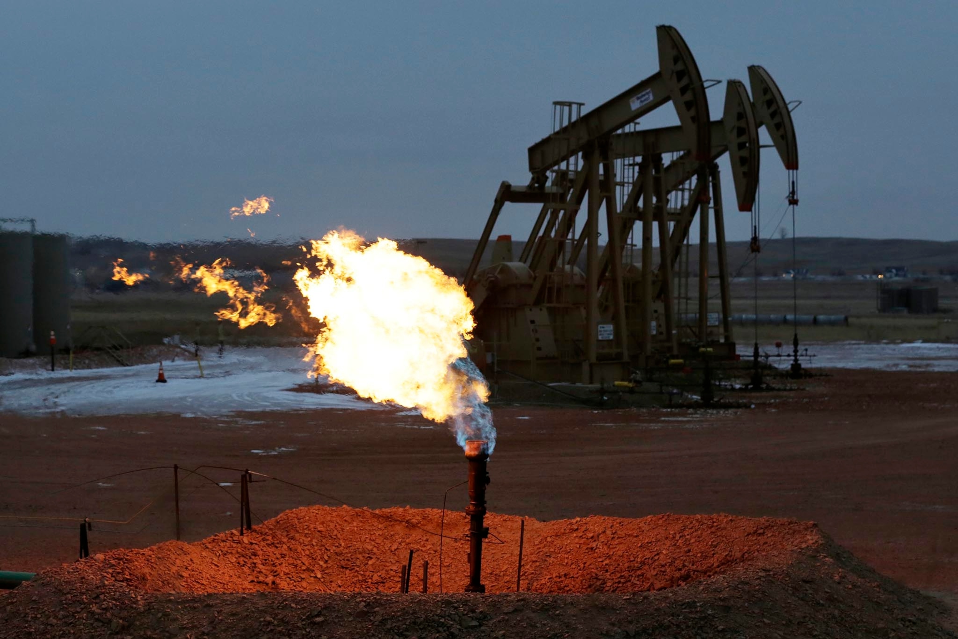 Oil pump jacks work behind a natural gas flare, Wednesday, Dec. 17, 2014, near Watford City, N.D. (AP Photo/Eric Gay)
