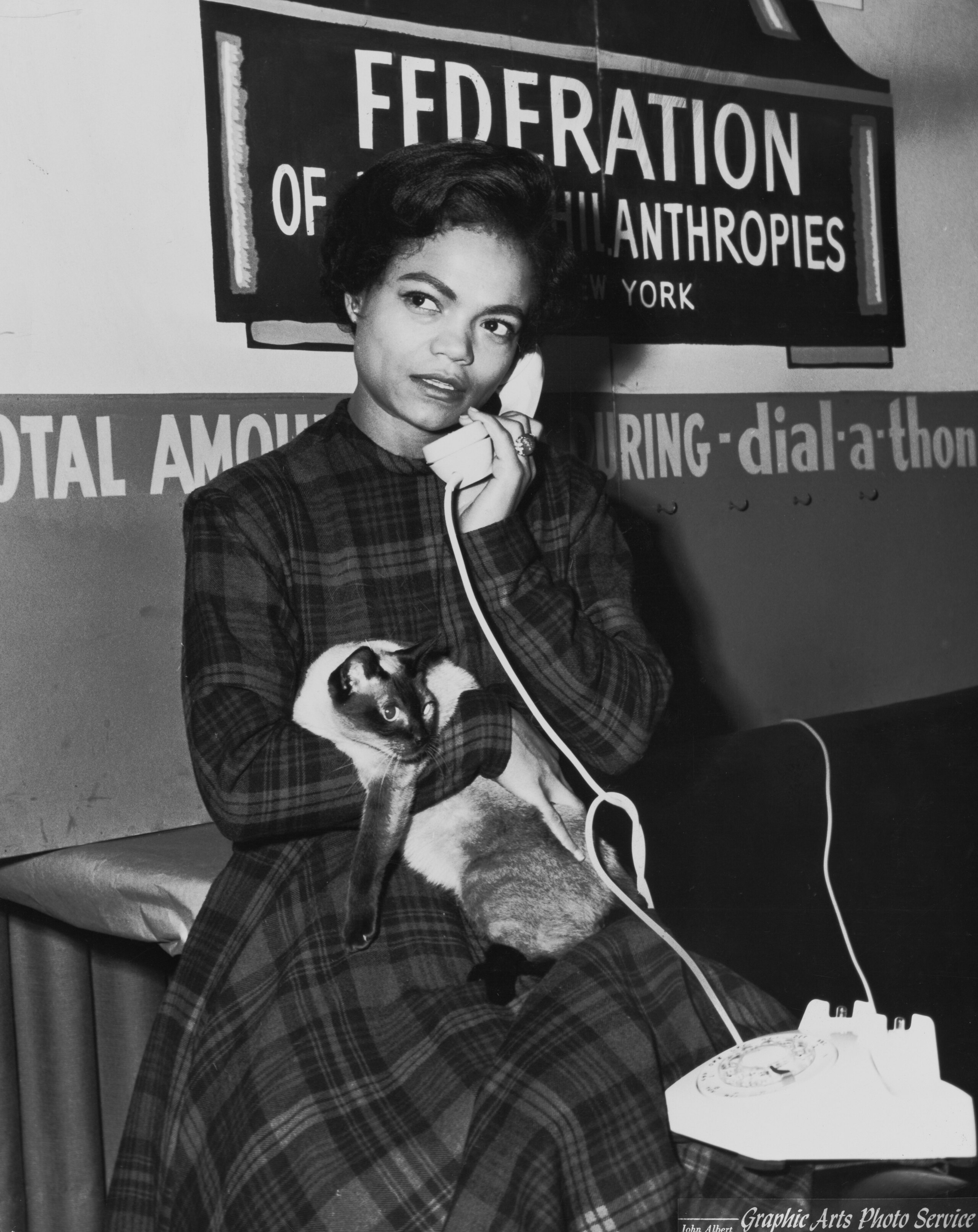 archival black and white photo of Eartha Kitt holding her Siamese cat while on a phone