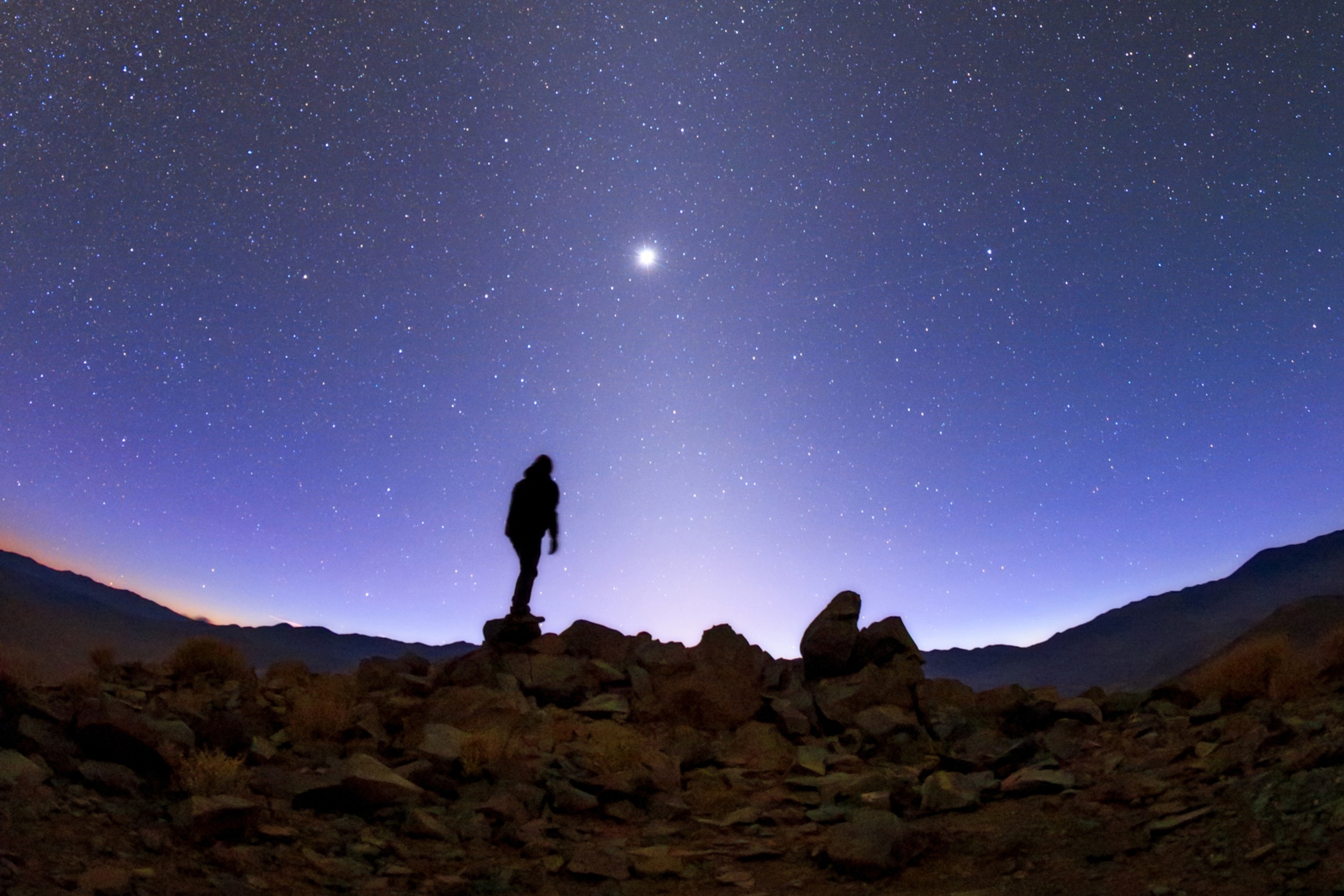 Silhouette of a person standing on rocky terrain under a vast, starry night sky