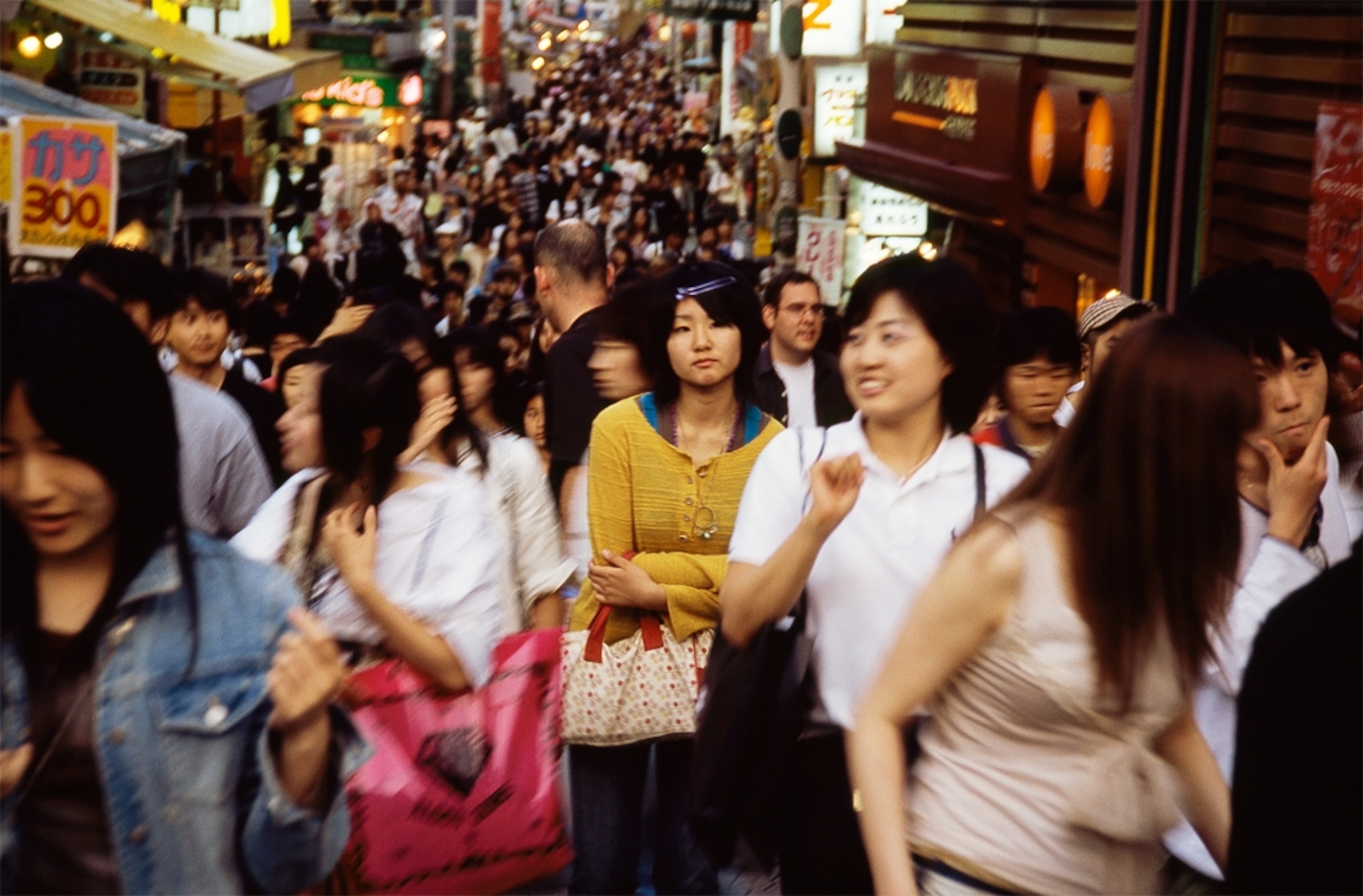People crowd a narrow street lined with shops in Tokyo