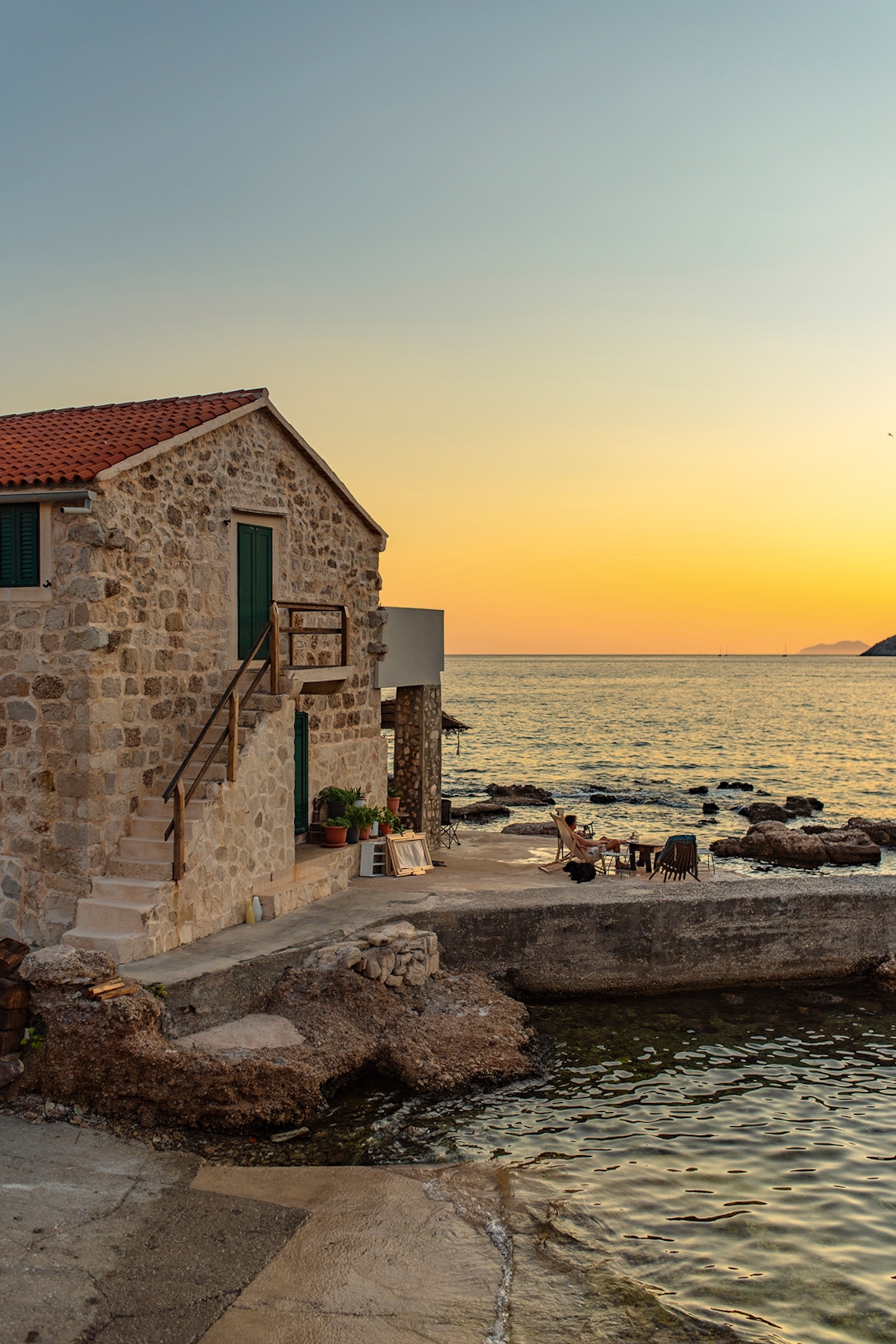 An old stone cottage on the shore of a sunset-lit sea.