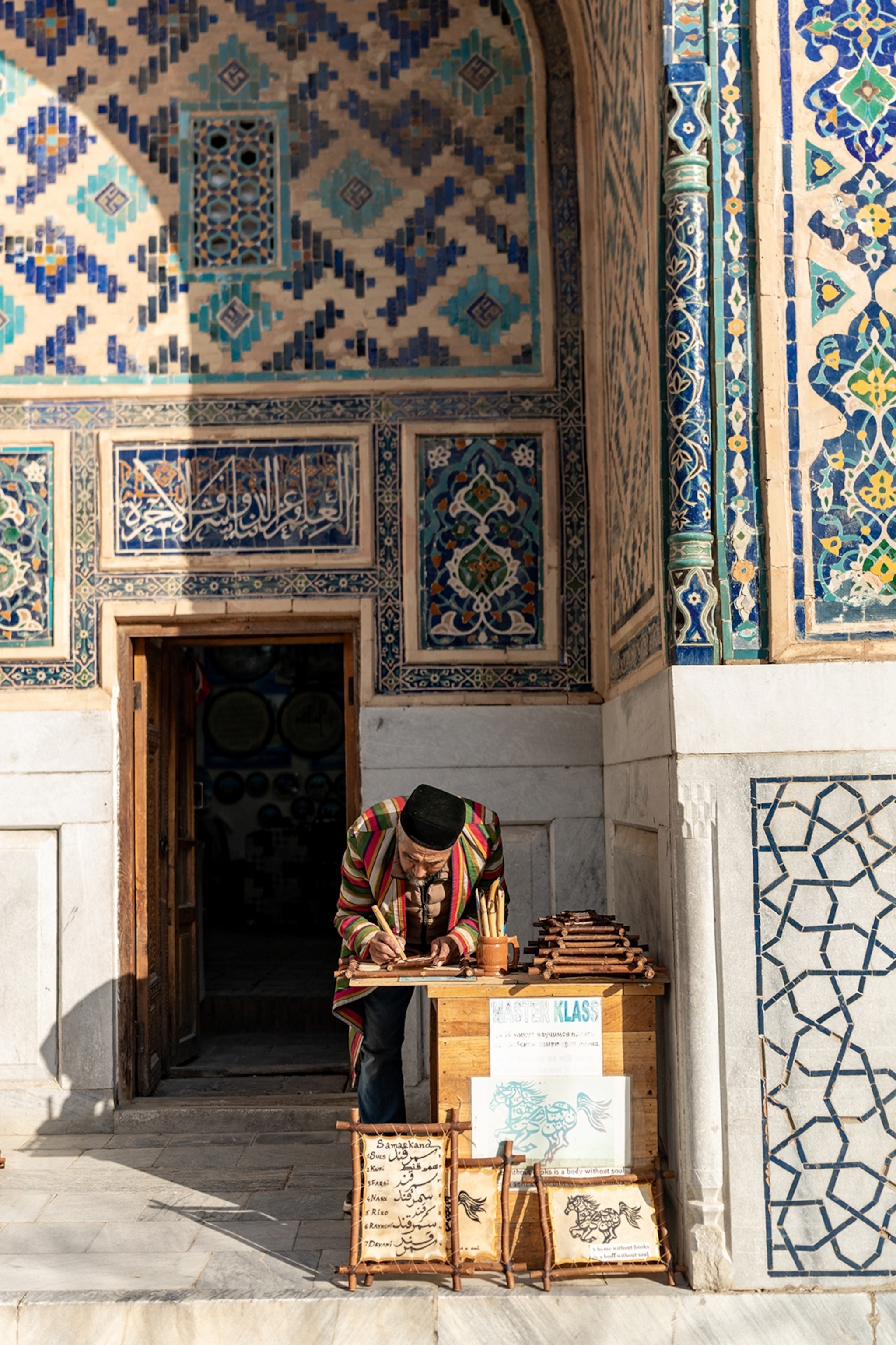 An elderly calligrapher sitting at a market stall in Uzbekistan.