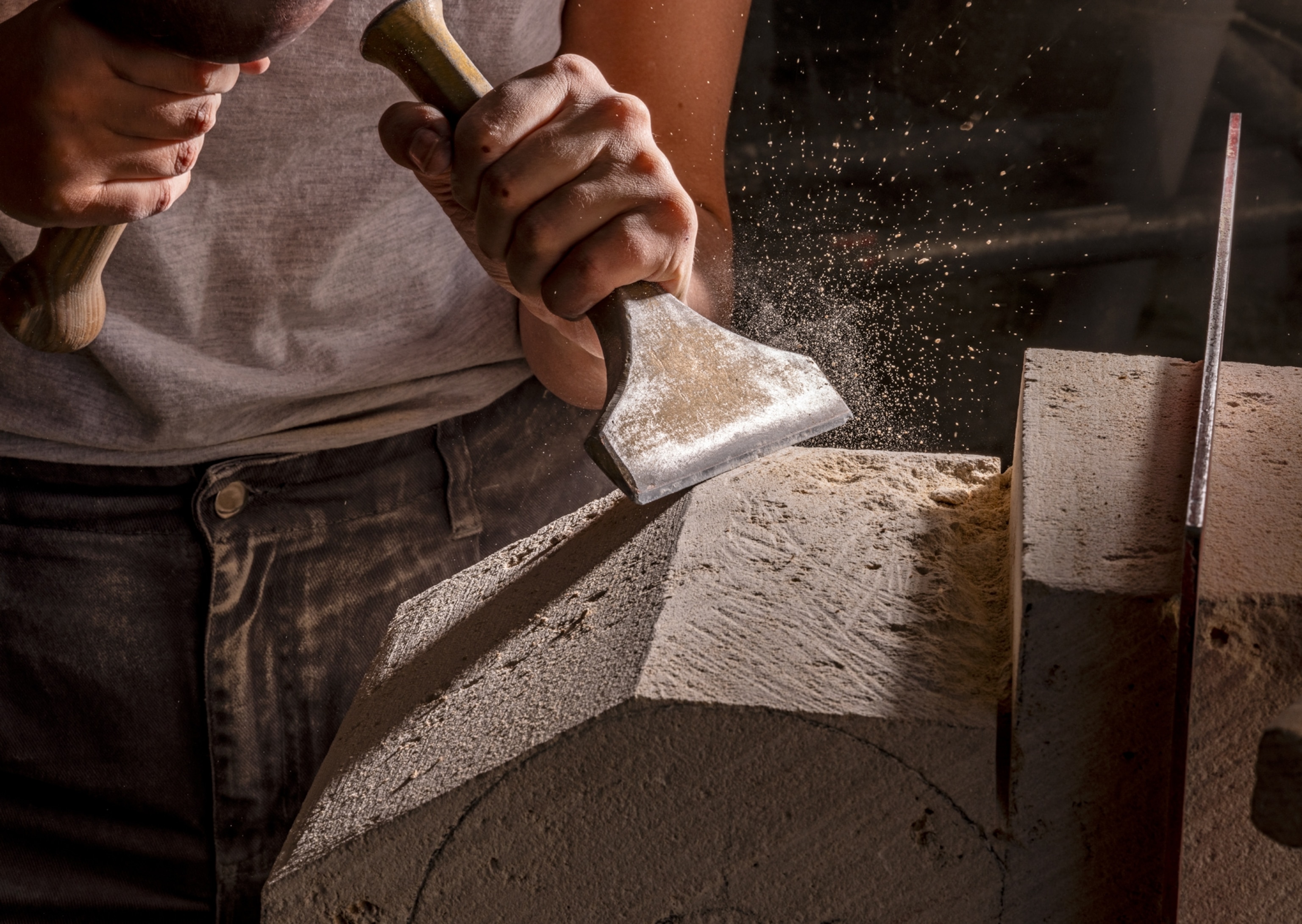 Hands working on block of stone with chisel and wooden mallet.
