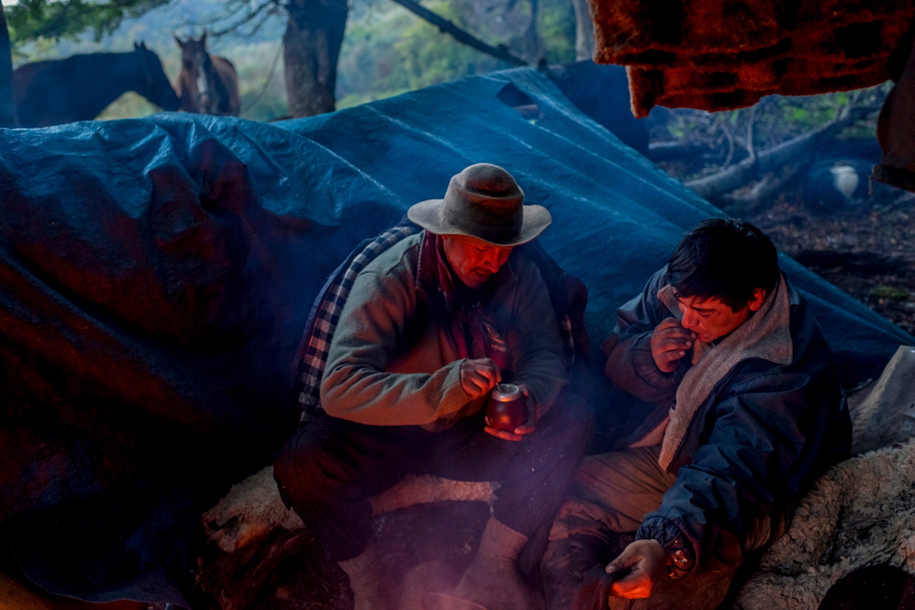 Bagualeros Abelino Torres (white hat), Dario Muñoz (black beret) and Jorge Vidal (blue beret) dry their clothes drinking mate, after a rainy day on the way to Sutherland in Peninsula Antonio Varas, Chilean Patagonia. January 9, 2014.