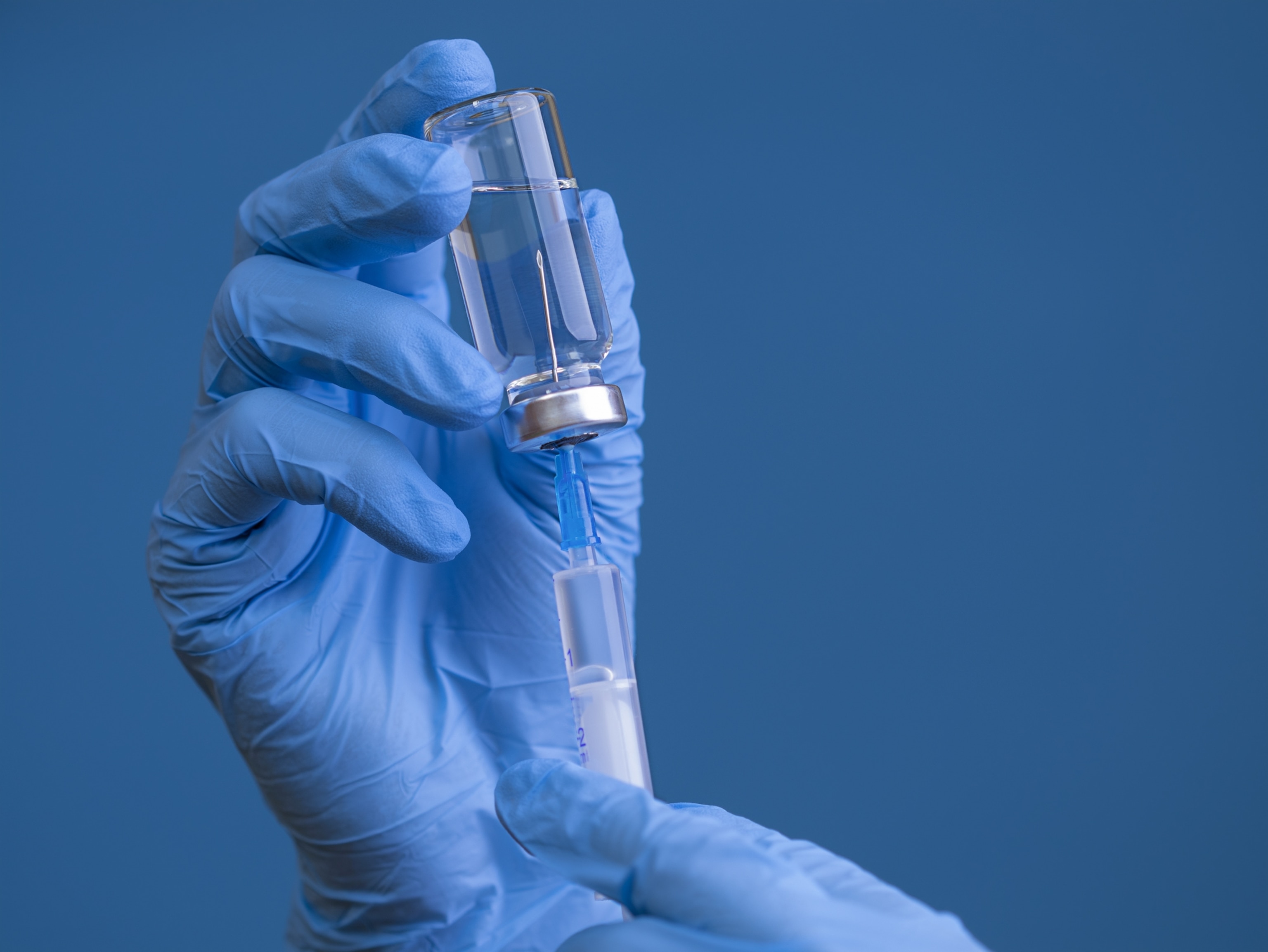 A gloved hand holds a vial and syringe against a blue background